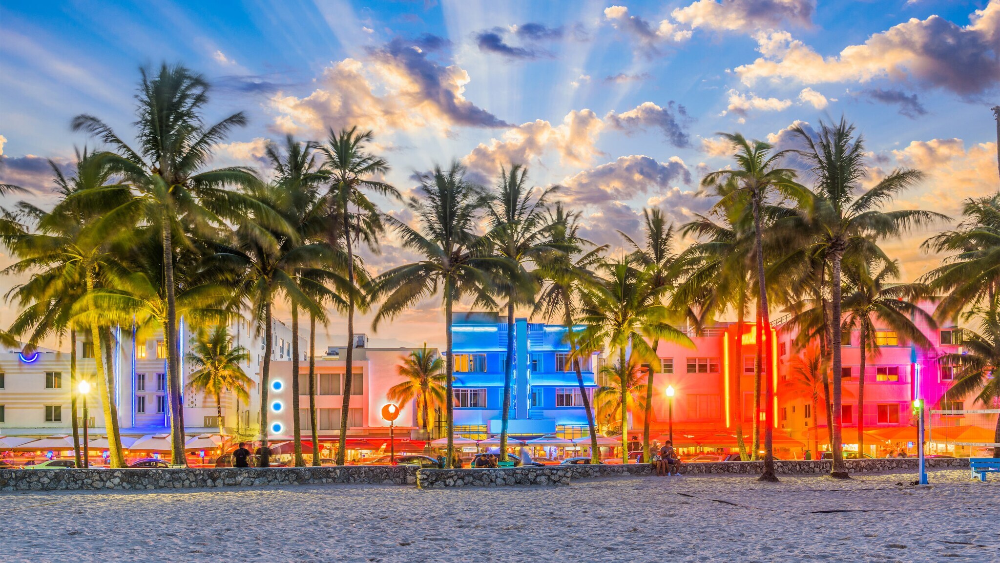 Strandpromenade mit Palmen und Art-déco-Gebäuden mit Neon-Beleuchtung am Abend.