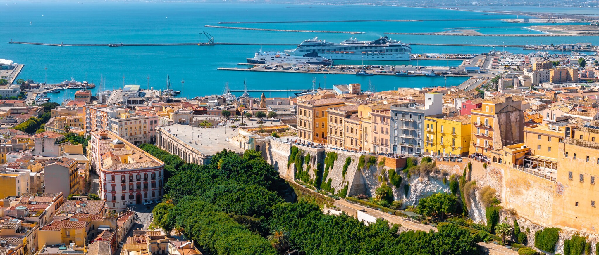 Panorama einer mediterranen Hafenstadt mit Kreuzfahrtschiff im Hintergrund.