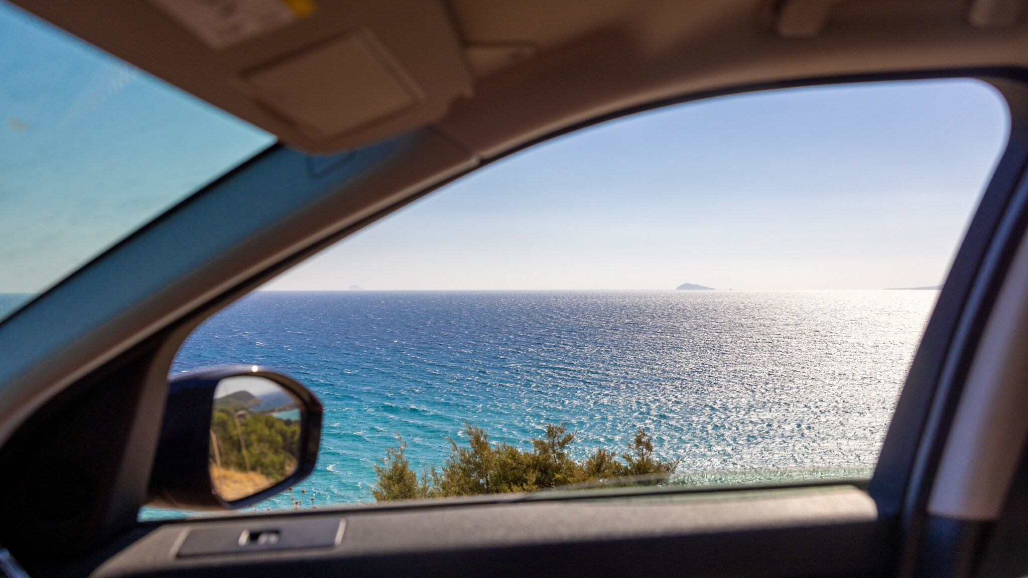 Meerblick durch ein geöffnetes Autofenster an einer Küste bei Sonnenschein.