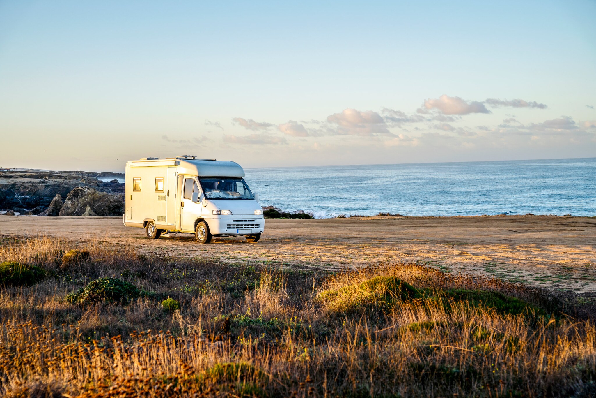 Ein Camper auf einer freien Fläche mit Sand an einer Küste bei Sonnenuntergang.