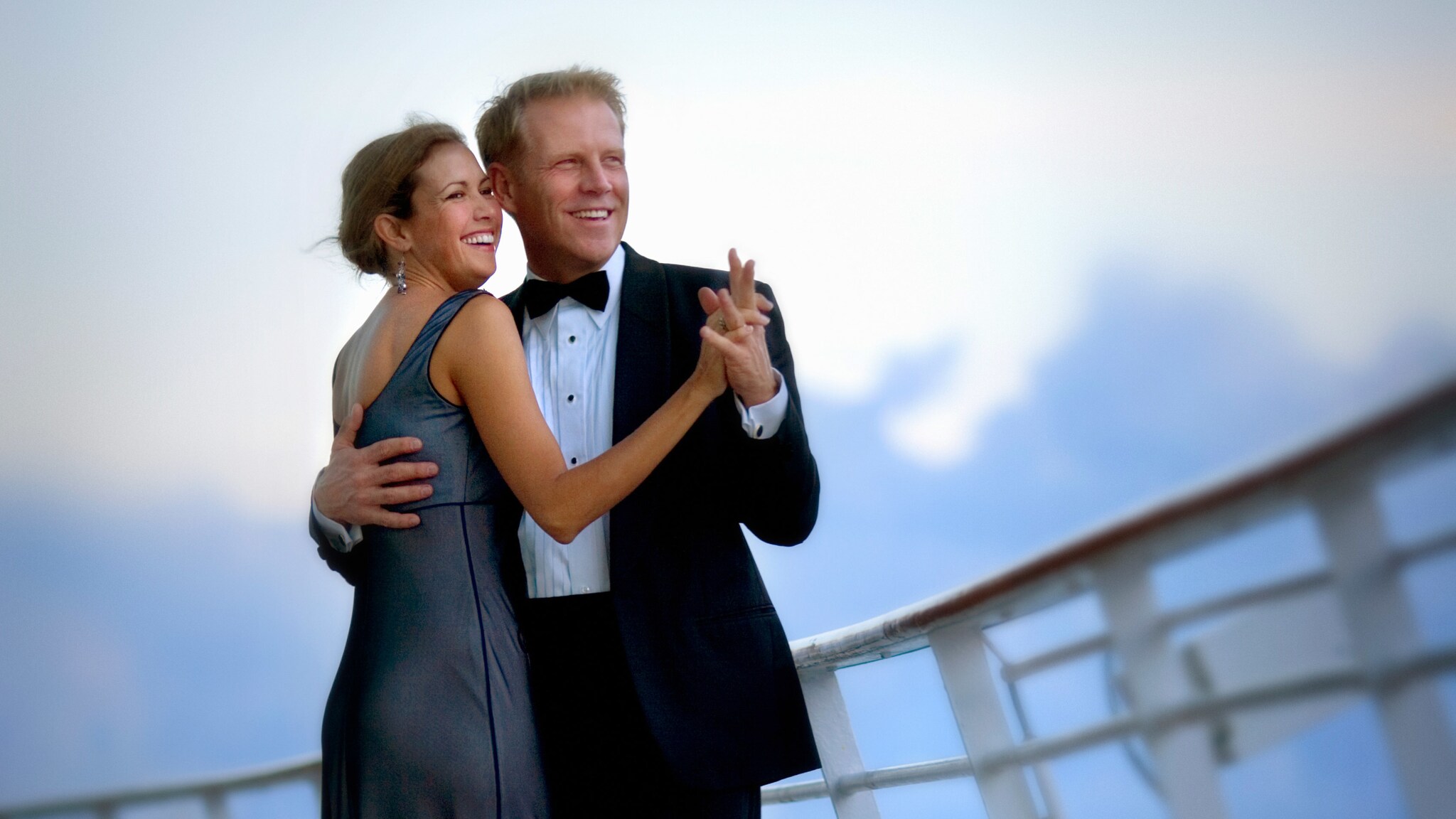 Ein tanzendes Paar in Abendgarderobe auf dem Außendeck eines Schiffes.