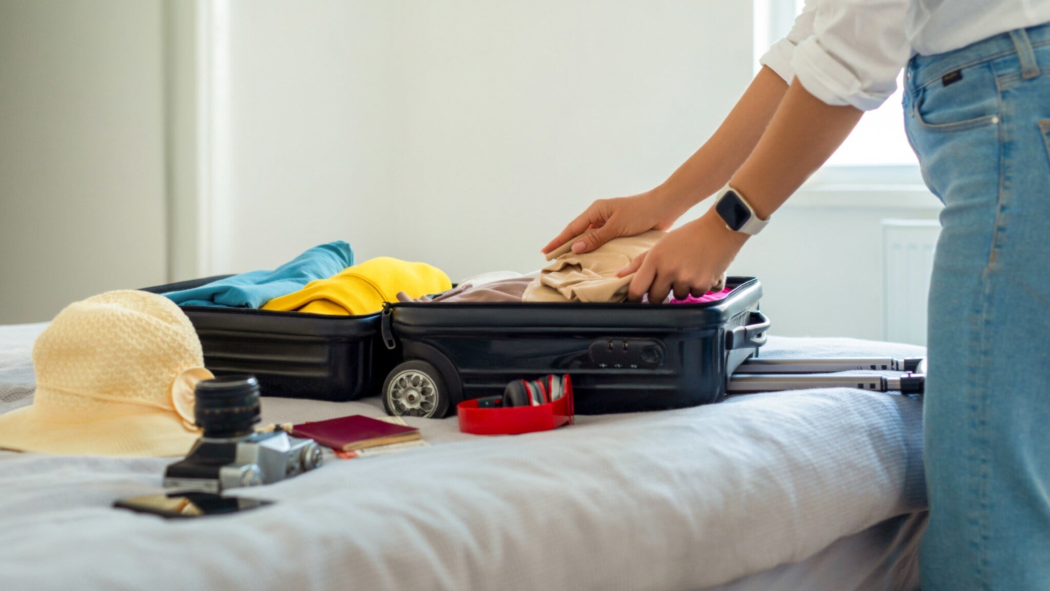 Eine Person bepackt einen Trolley auf einem Bett für eine Sommerreise. Eine Person bepackt einen Trolley auf einem Bett für eine Sommerreise.