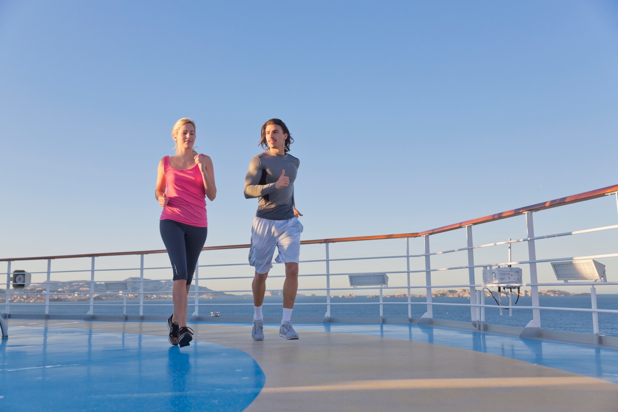 Ein Paar in Sportkleidung läuft auf dem Deck eines Kreuzfahrtschiffes auf See. Ein Paar in Sportkleidung läuft auf dem Deck eines Kreuzfahrtschiffes auf See.