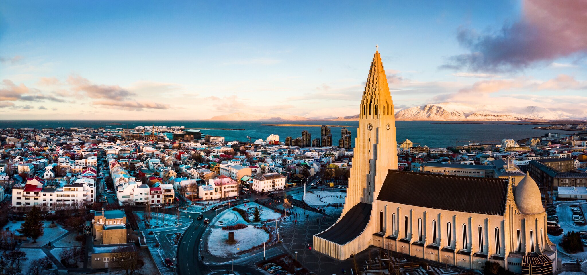 Skyline von Reykjavik mit Pfarrkirche vor Meerespanorama mit schneebedeckten Bergen.