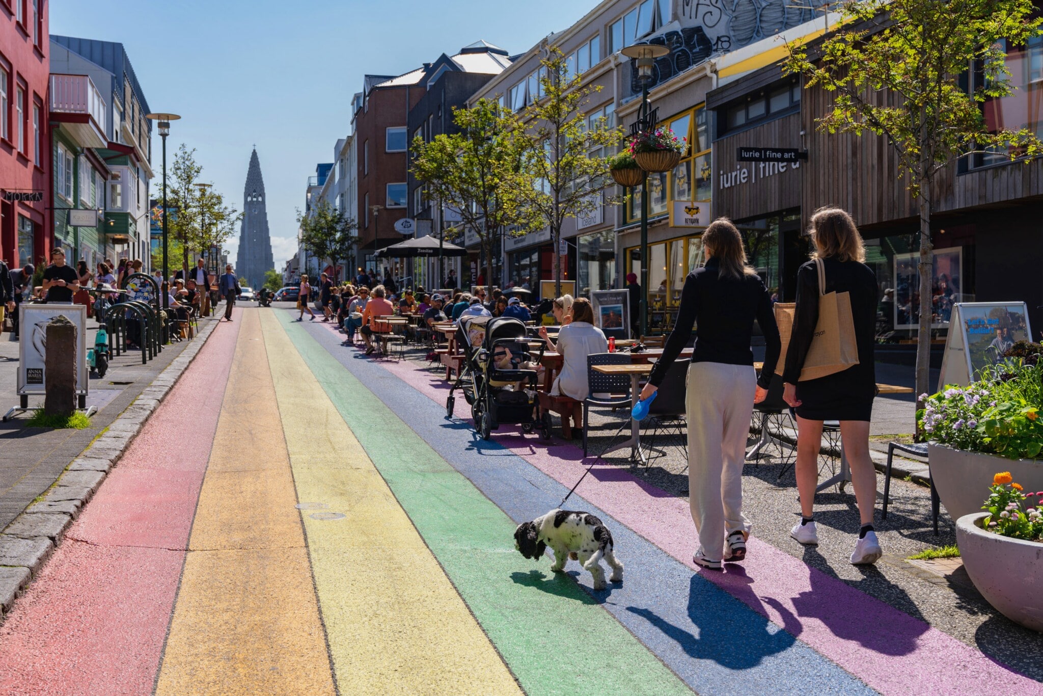 Personen auf einer Einkaufsstraße mit Regenbogenfarben auf dem Asphalt bei Sonnenschein. Personen auf einer Einkaufsstraße mit Regenbogenfarben auf dem Asphalt bei Sonnenschein.