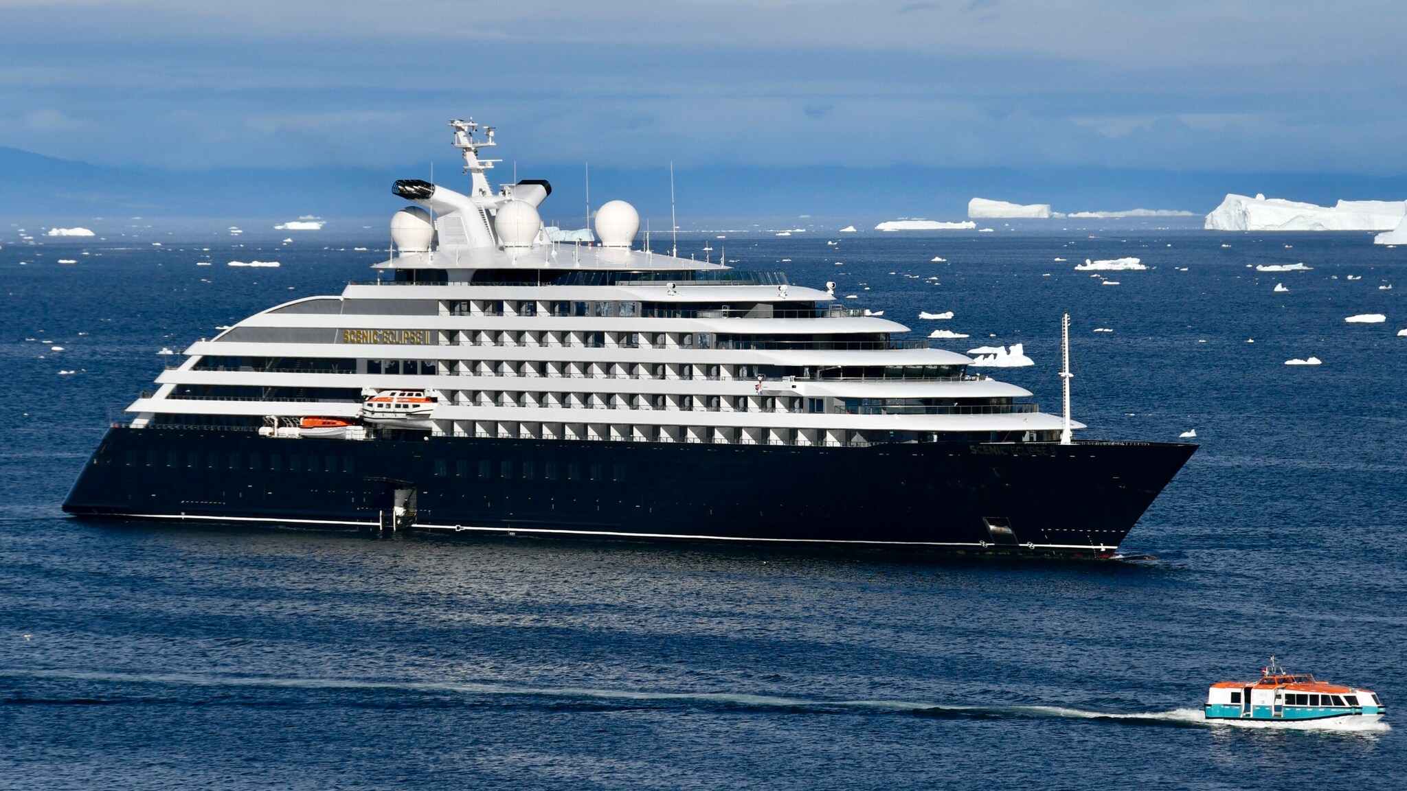 Das Bild zeigt das Expeditionskreuzfahrtschiff Scenic Eclipse II umgeben von kleinen und großen Eisbergen und einem Tenderboot im Vordergrund.