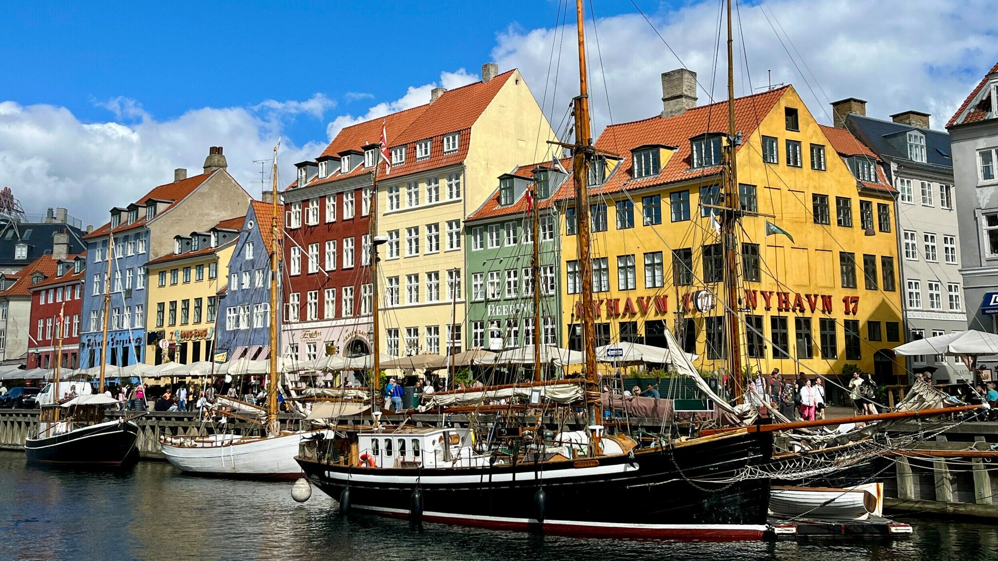 Das Bild zeigt eine Reihe in verschiedenen Farben angestrichener Häuser. Im Kanal davor liegen historische Schiffe. Das Bild zeigt eine Reihe in verschiedenen Farben angestrichener Häuser. Im Kanal davor liegen historische Schiffe.