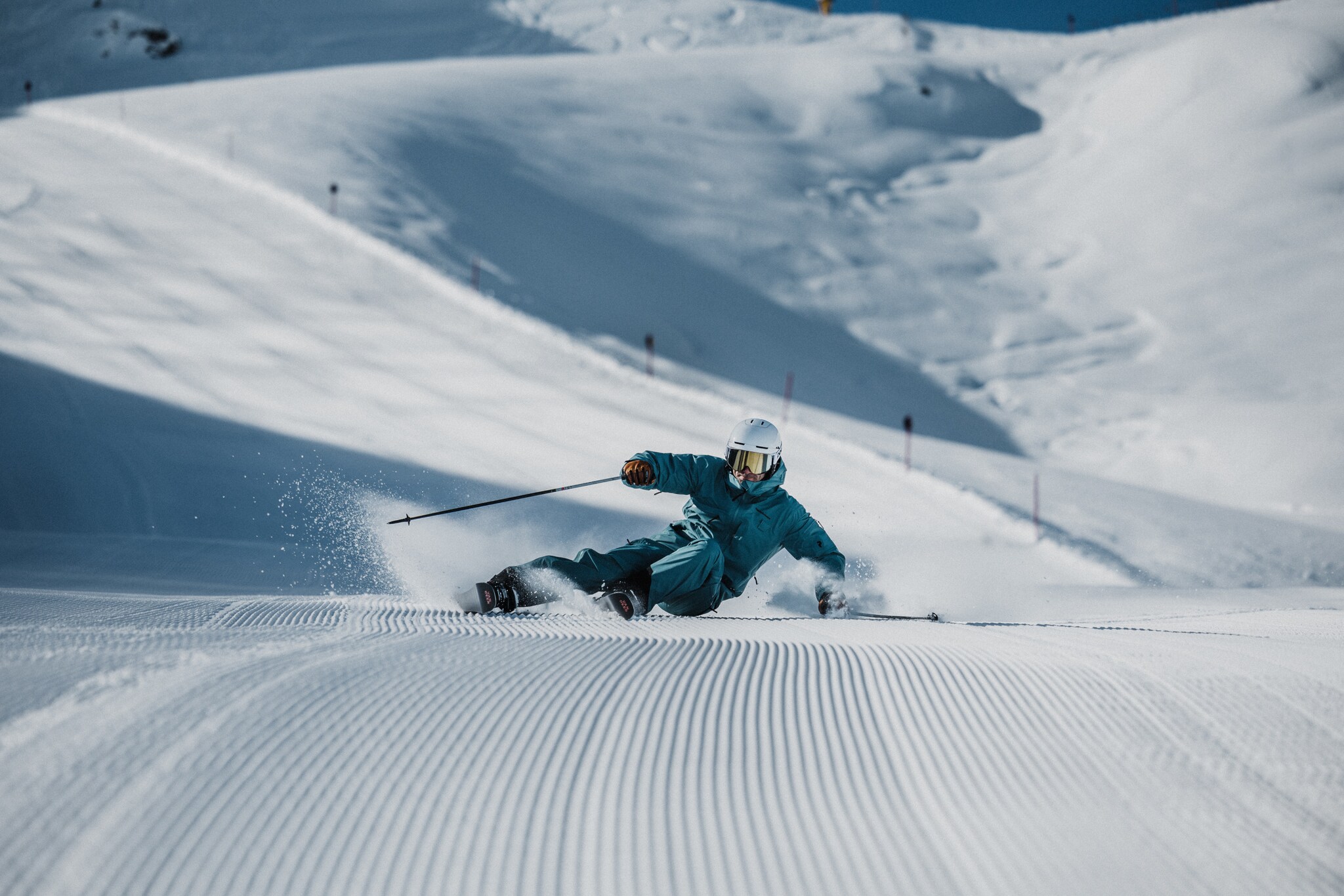 Ein Skifahrer mit Helm im türkisen Schneeanzug bei der Abfahrt auf einer Piste.
