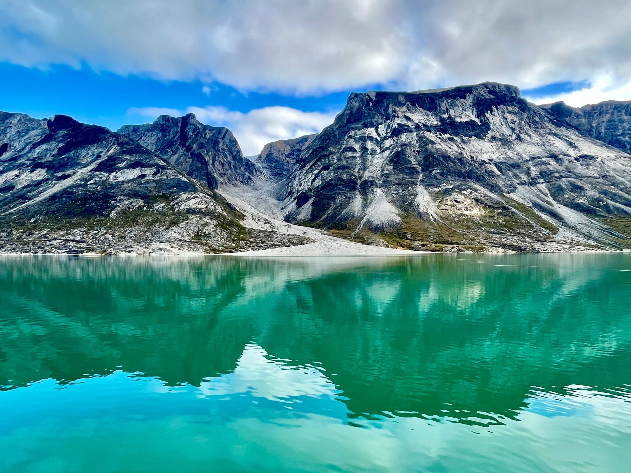 Das Bild zeigt dunkle Berge, die aus dem grün schimmernden Wasser des Prins Christian Sunds ragen.