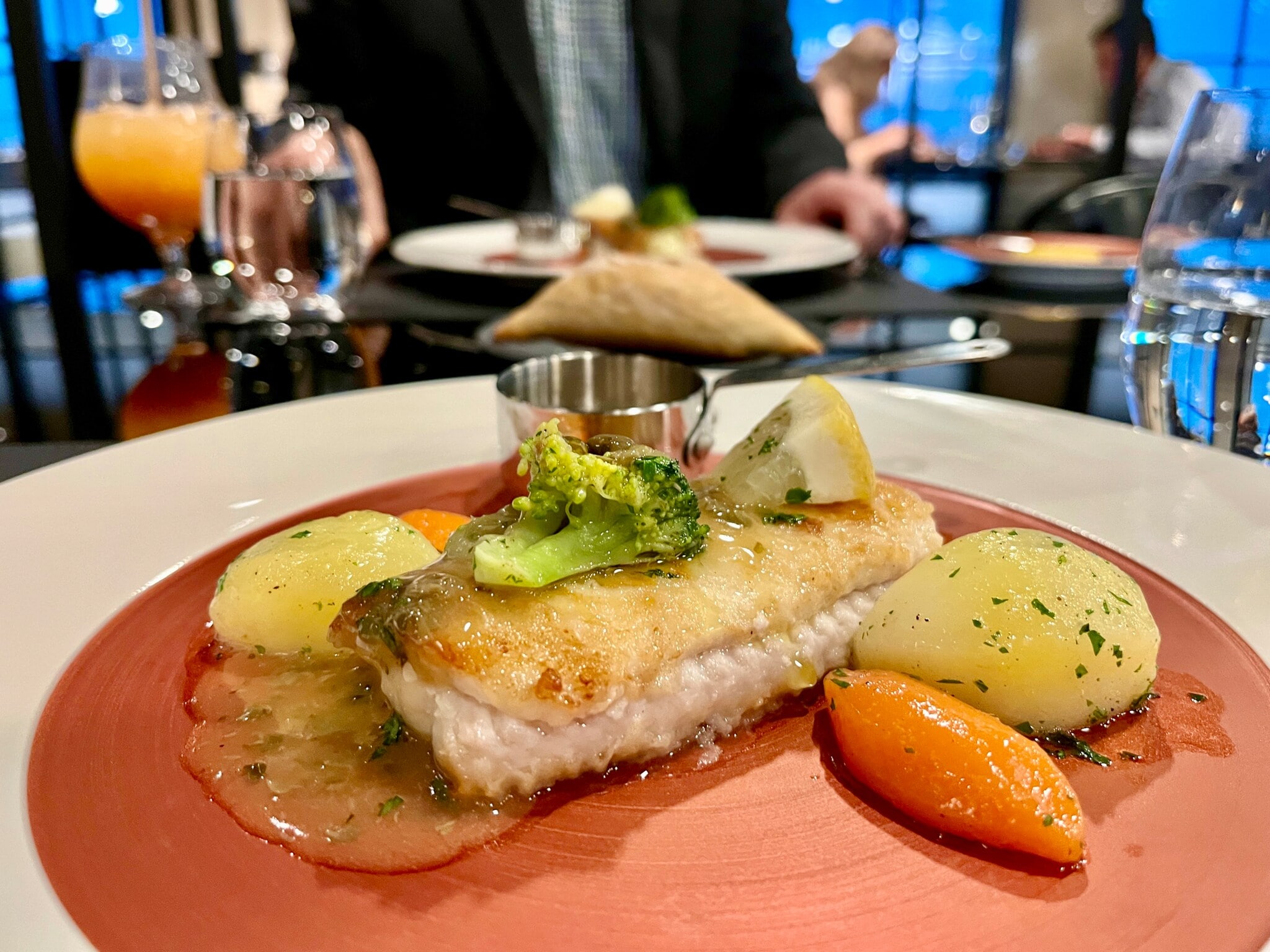 Das Bild zeigt ein Fischgericht auf einem bronze-weißen Teller. Der Fisch wird mit Kartoffeln, Möhren, Broccoli und Zitrone serviert. Das Bild zeigt ein Fischgericht auf einem bronze-weißen Teller. Der Fisch wird mit Kartoffeln, Möhren, Broccoli und Zitrone serviert.