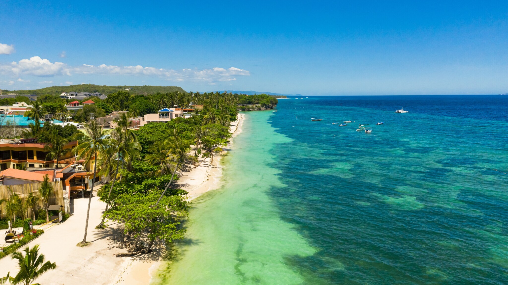 Bungalows auf einem palmengesäumten Sandstrand an türkisblauer Meeresküste.