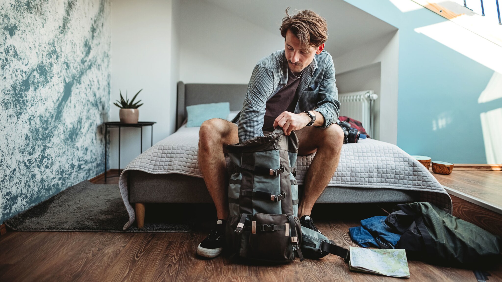 Ein Mann sitzt auf einem Bett und packt einen großen Rucksack. Ein Mann sitzt auf einem Bett und packt einen großen Rucksack.