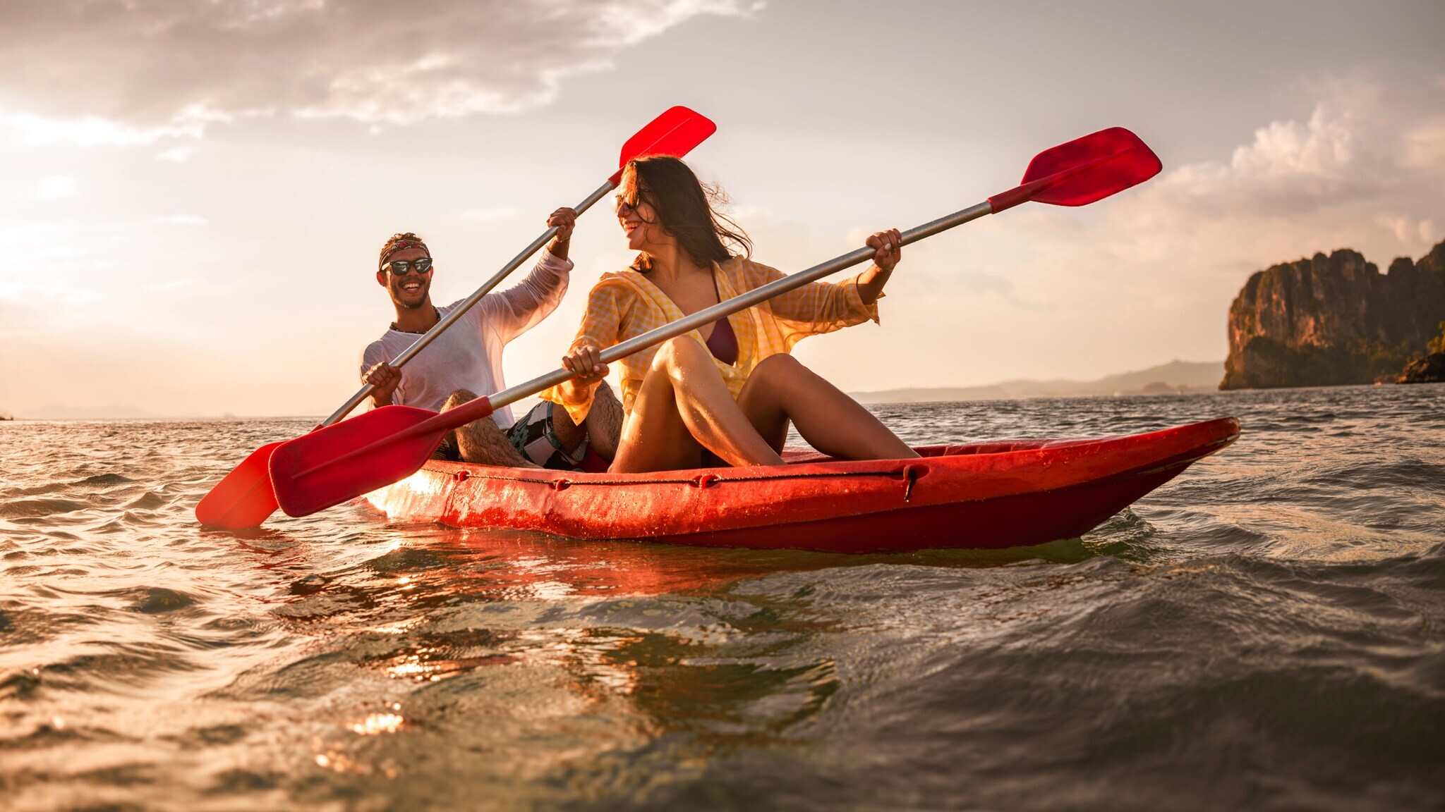 Zwei glückliche Personen, die bei Sonnenuntergang in einem Kajak auf dem Wasser sitzen und jeweils ein Padel halten.
