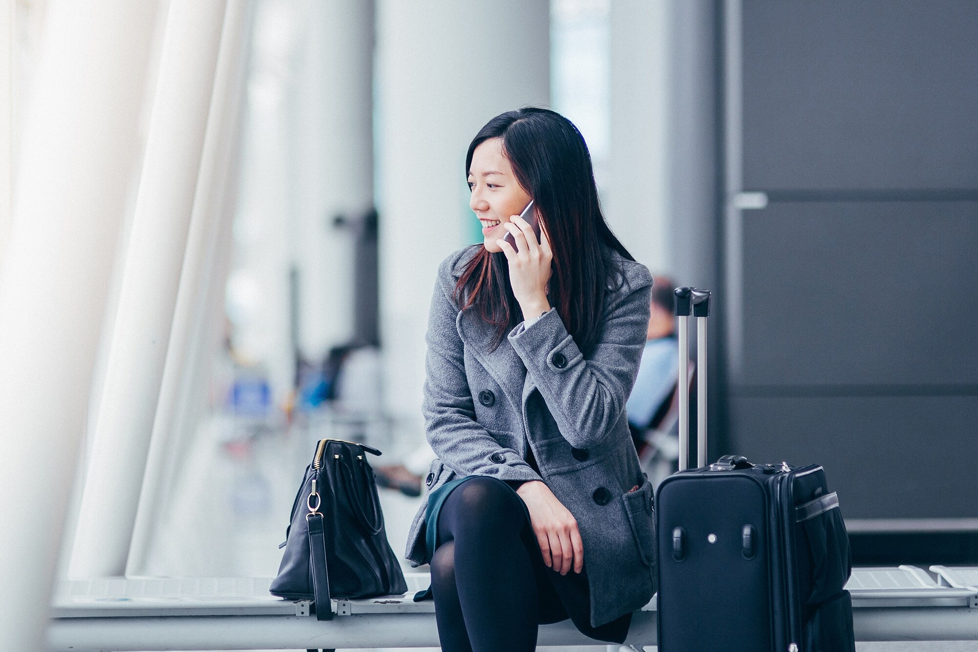Dienstreise ins Ausland: 6 Tipps für den Erfolg Eine asiatische Geschäftsfrau sitzt im Wartebereich eines Flughafens und telefoniert.