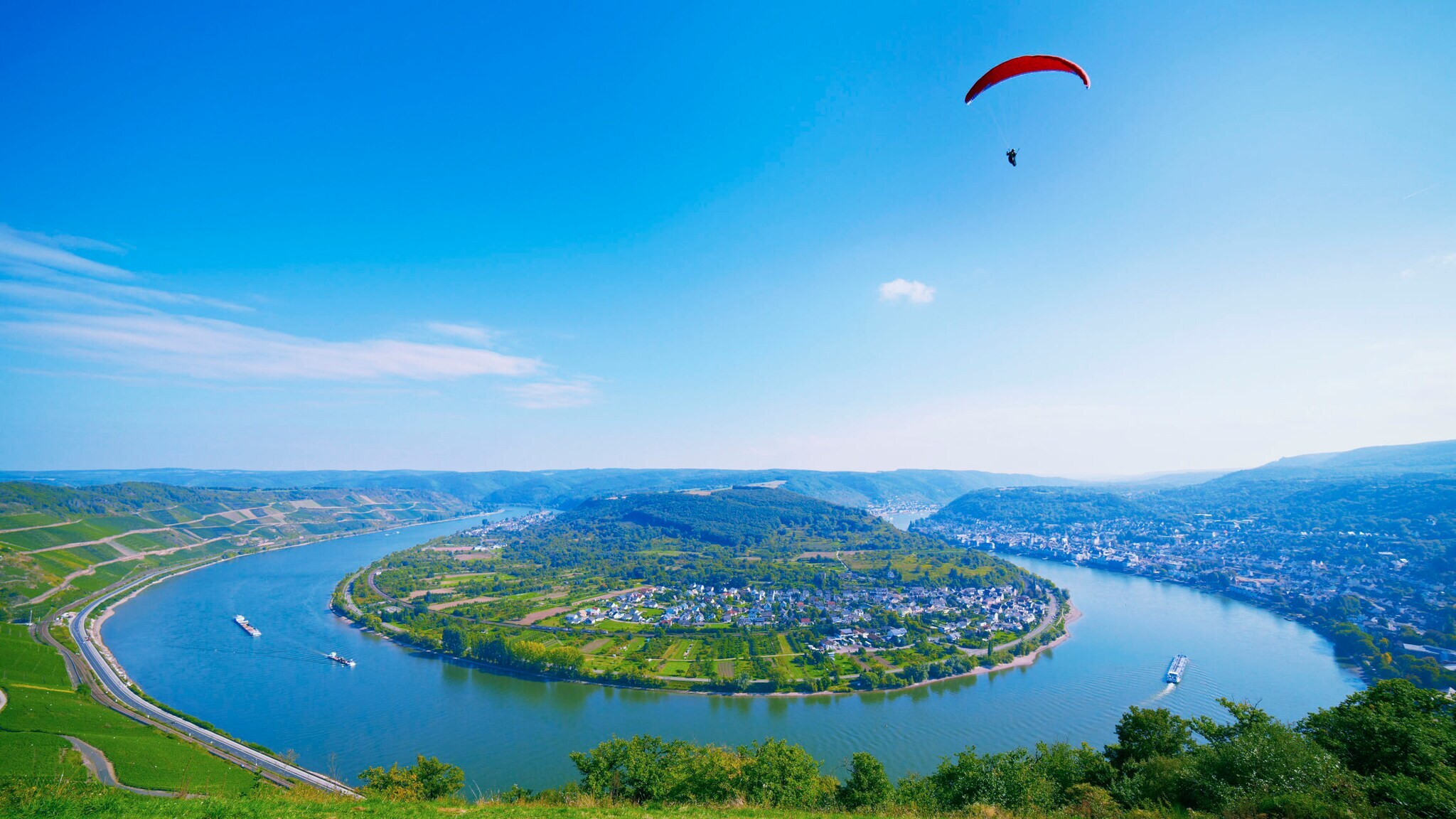 Panoramaaufnahme der Rheinschleife bei Boppard, über die eine Person mit Gleitschirm in der Ferne schwebt