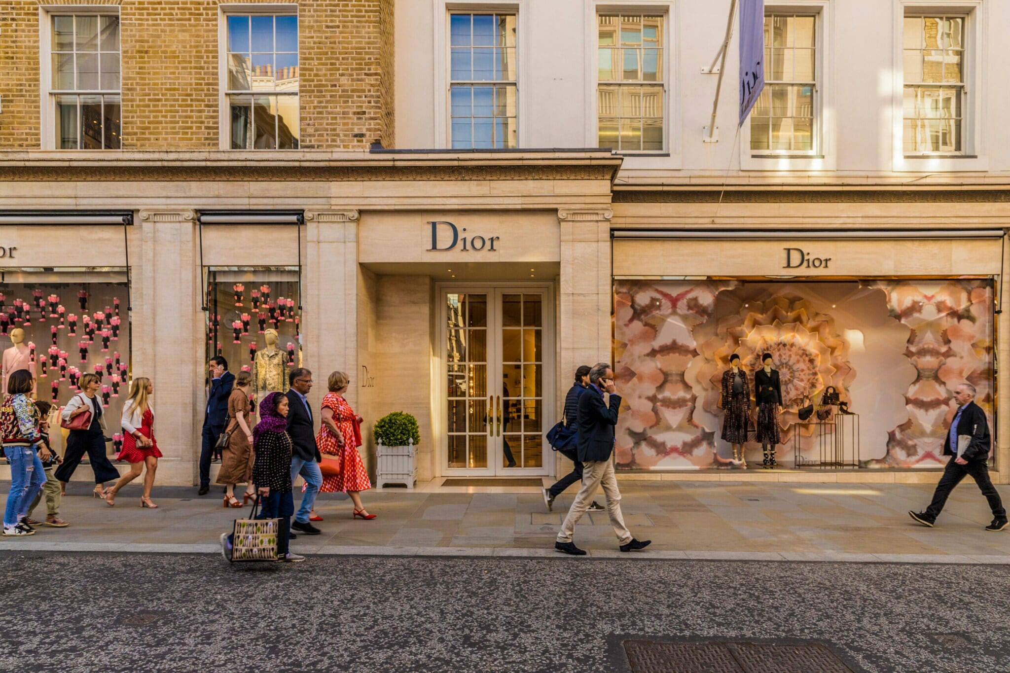 Passanten vor einer edlen Dior Modeboutique mit dekorierten Schaufenstern in einer Einkaufsstraße. Passanten vor einer edlen Dior Modeboutique mit dekorierten Schaufenstern in einer Einkaufsstraße.