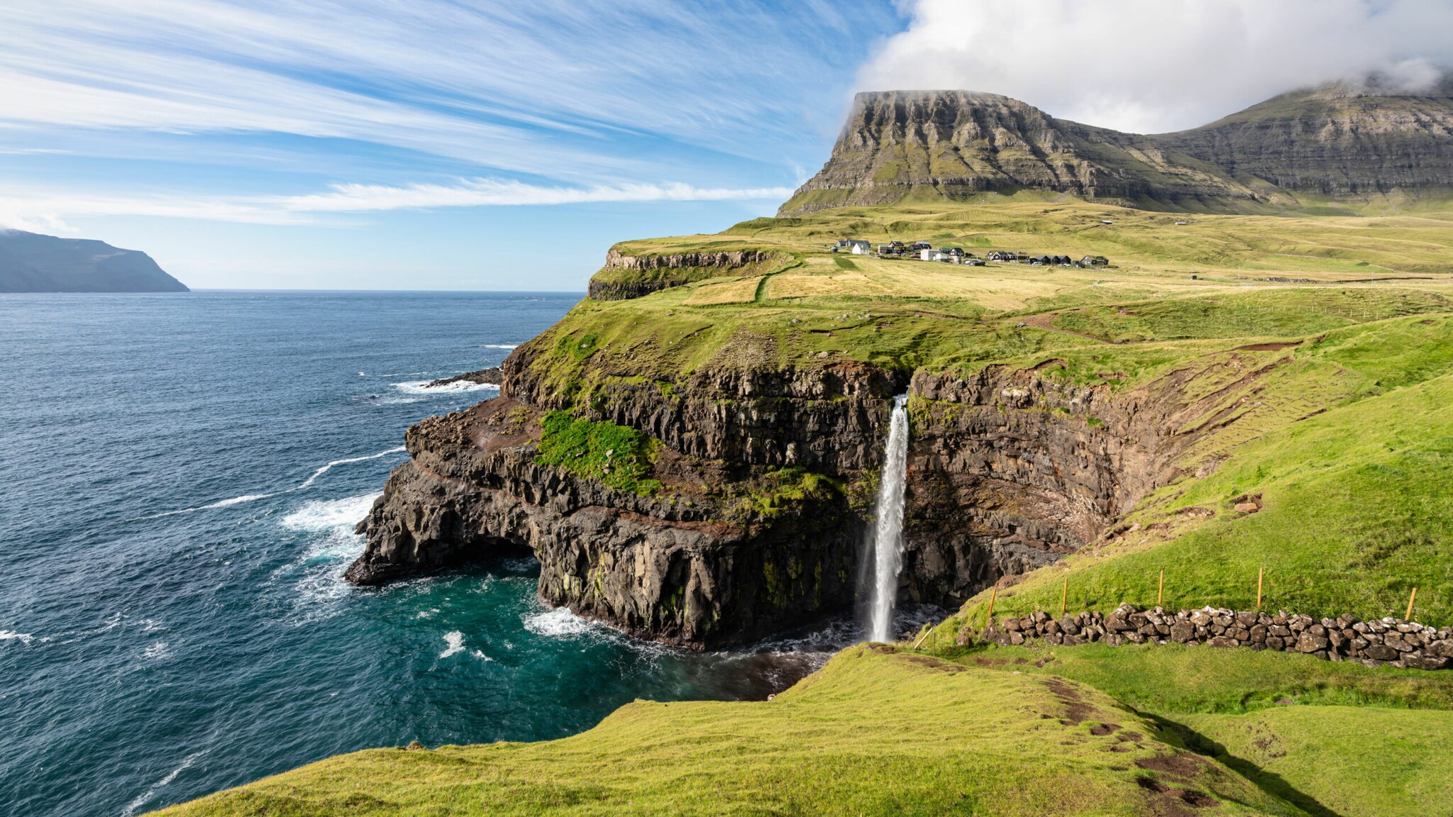 Ein Wasserfall auf einer mit Gras bewachsenen Felseninsel stürzt eine Klippe hinab ins Meer.