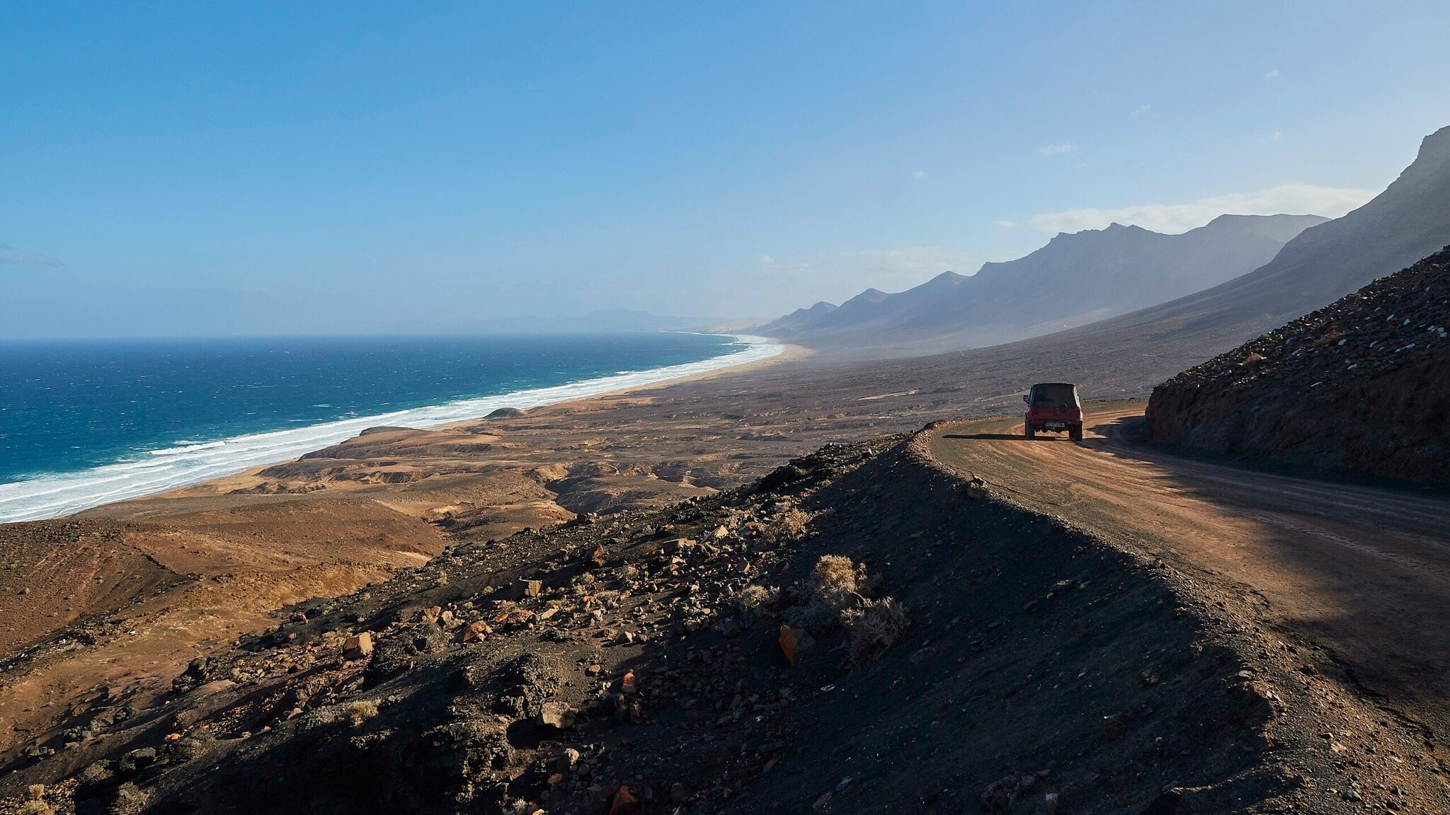 Ein Jeep fährt auf einer unbefestigten durch eine gebirgige Wüstenlandschaft am Meer. Ein Jeep fährt auf einer unbefestigten durch eine gebirgige Wüstenlandschaft am Meer.