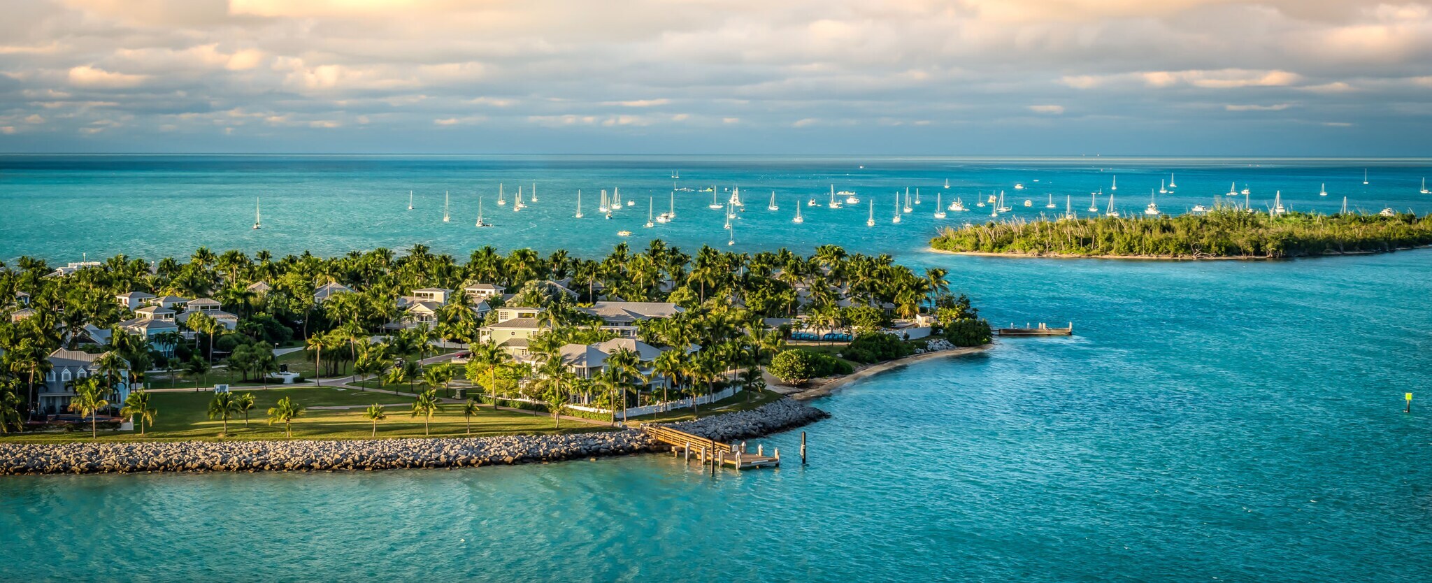 Zwei kleine Inseln mit weißen Häusern und Palmen, im Hintergrund zahlreiche Segelboote im türkisblauen Meer.