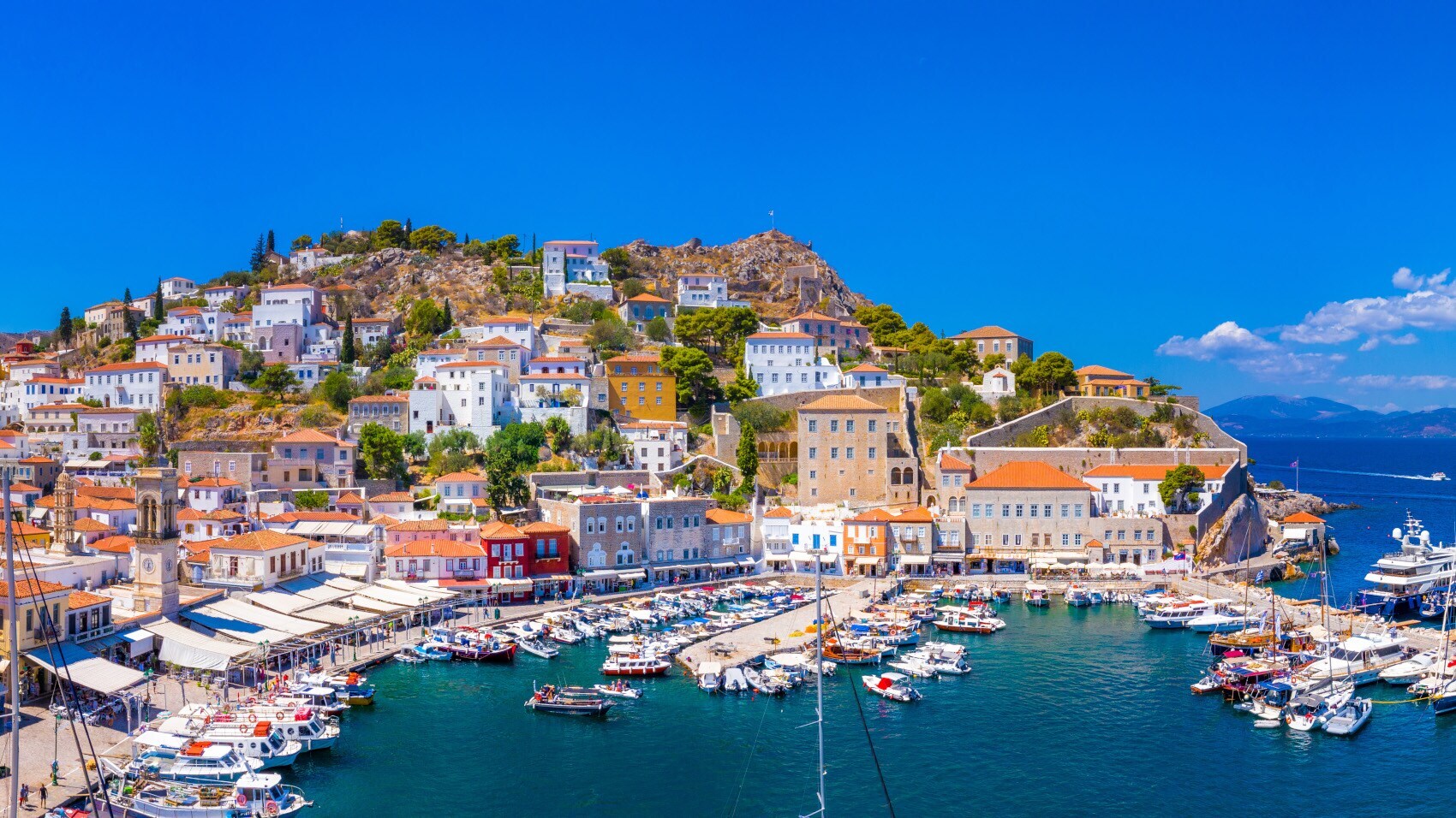 Mediterrane Ortschaft in Hanglage am Meer mit Hafenpromenade und Fischerbooten.