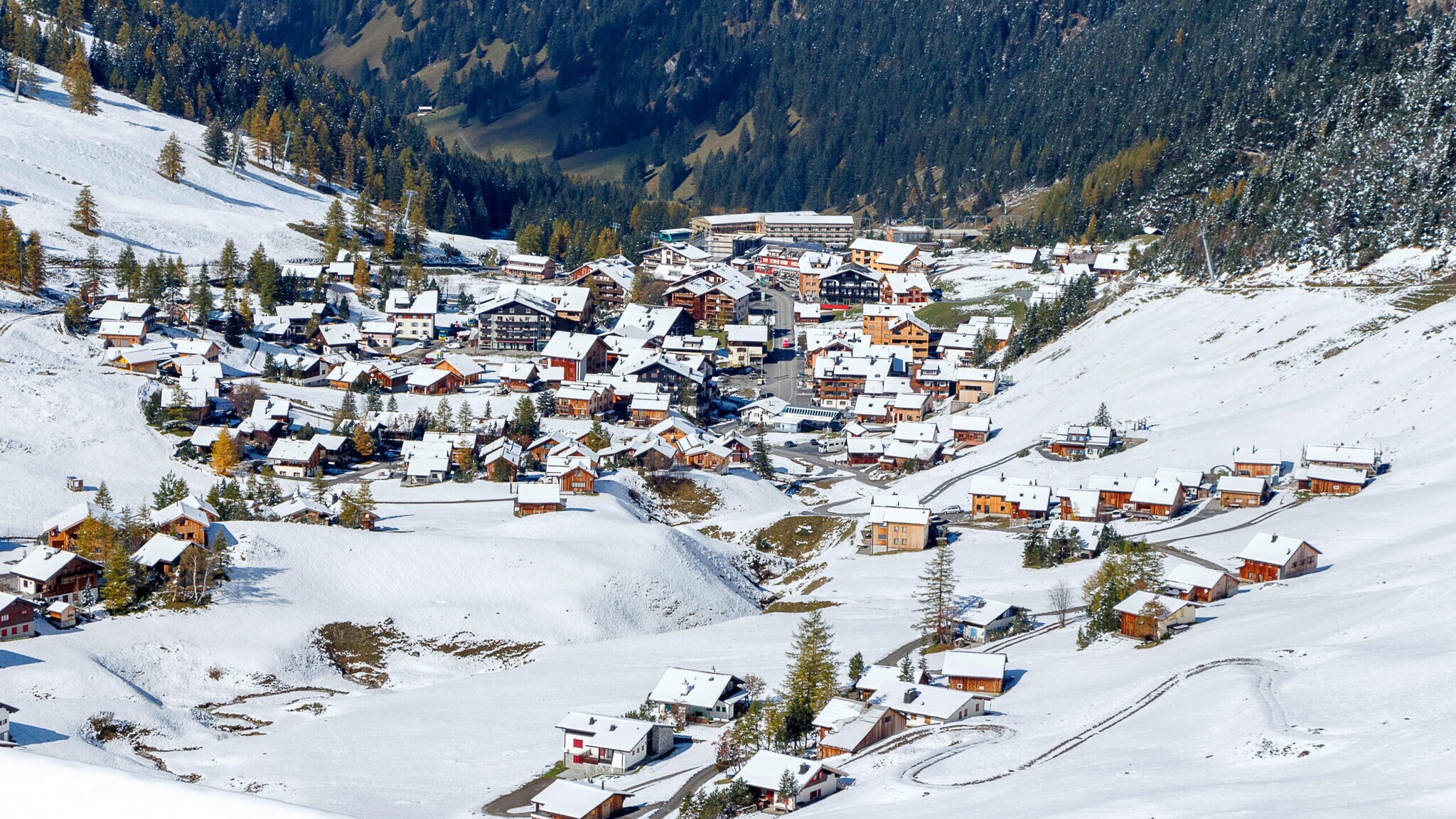 Schneebedeckter Ort in einem Tal, umgeben von bewaldeten Bergen. Schneebedeckter Ort in einem Tal, umgeben von bewaldeten Bergen.