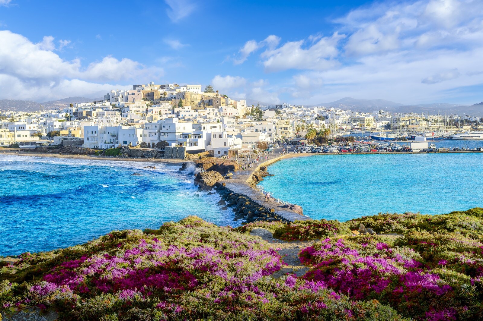 Griechische Kleinstadt mit weißen Häusern und Kaimauer am türkisblauen Meer, im Vordergrund ein bewachsener Hügel. Griechische Kleinstadt mit weißen Häusern und Kaimauer am türkisblauen Meer, im Vordergrund ein bewachsener Hügel.