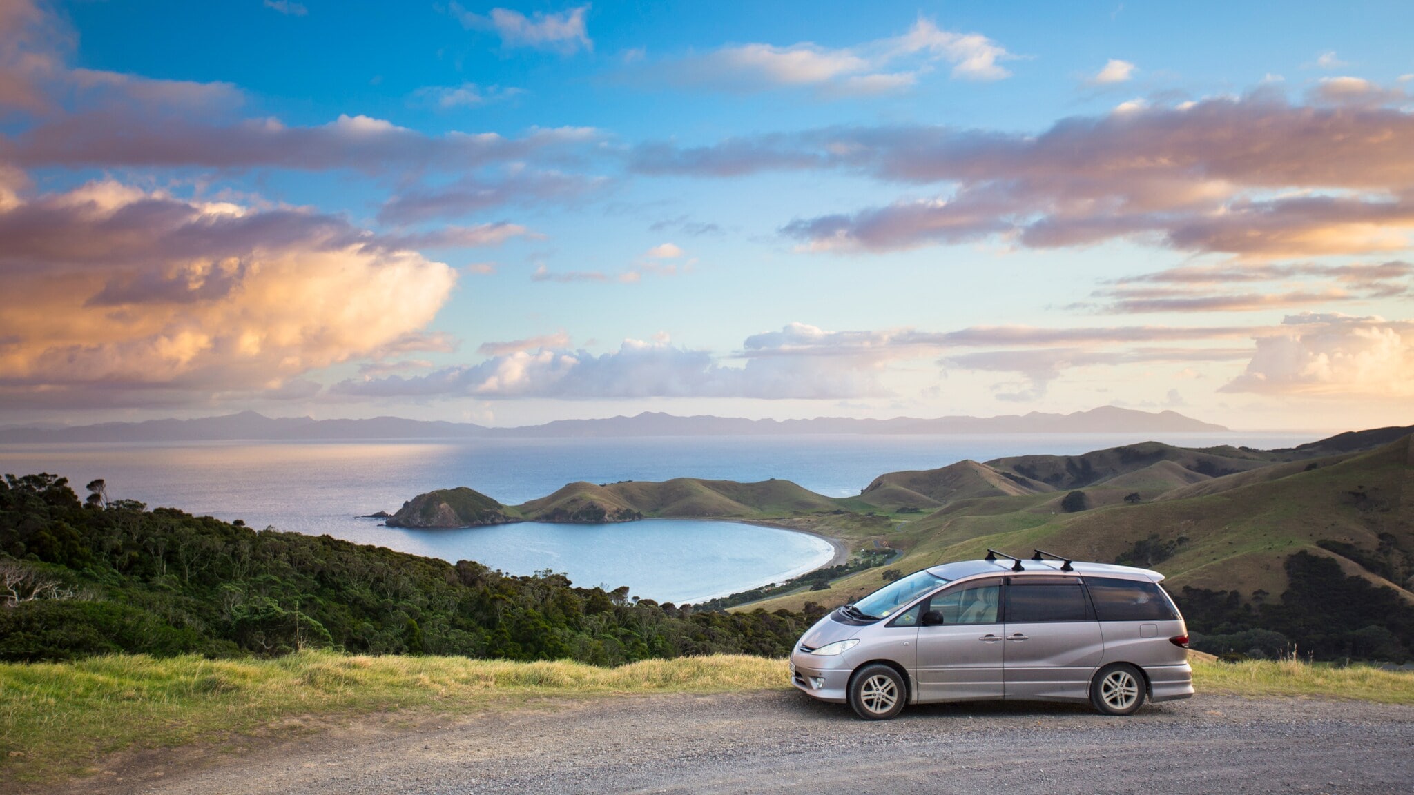 Ein silberner Van vor Küstenpanorama mit grüner Hügellandschaft. Ein silberner Van vor Küstenpanorama mit grüner Hügellandschaft.