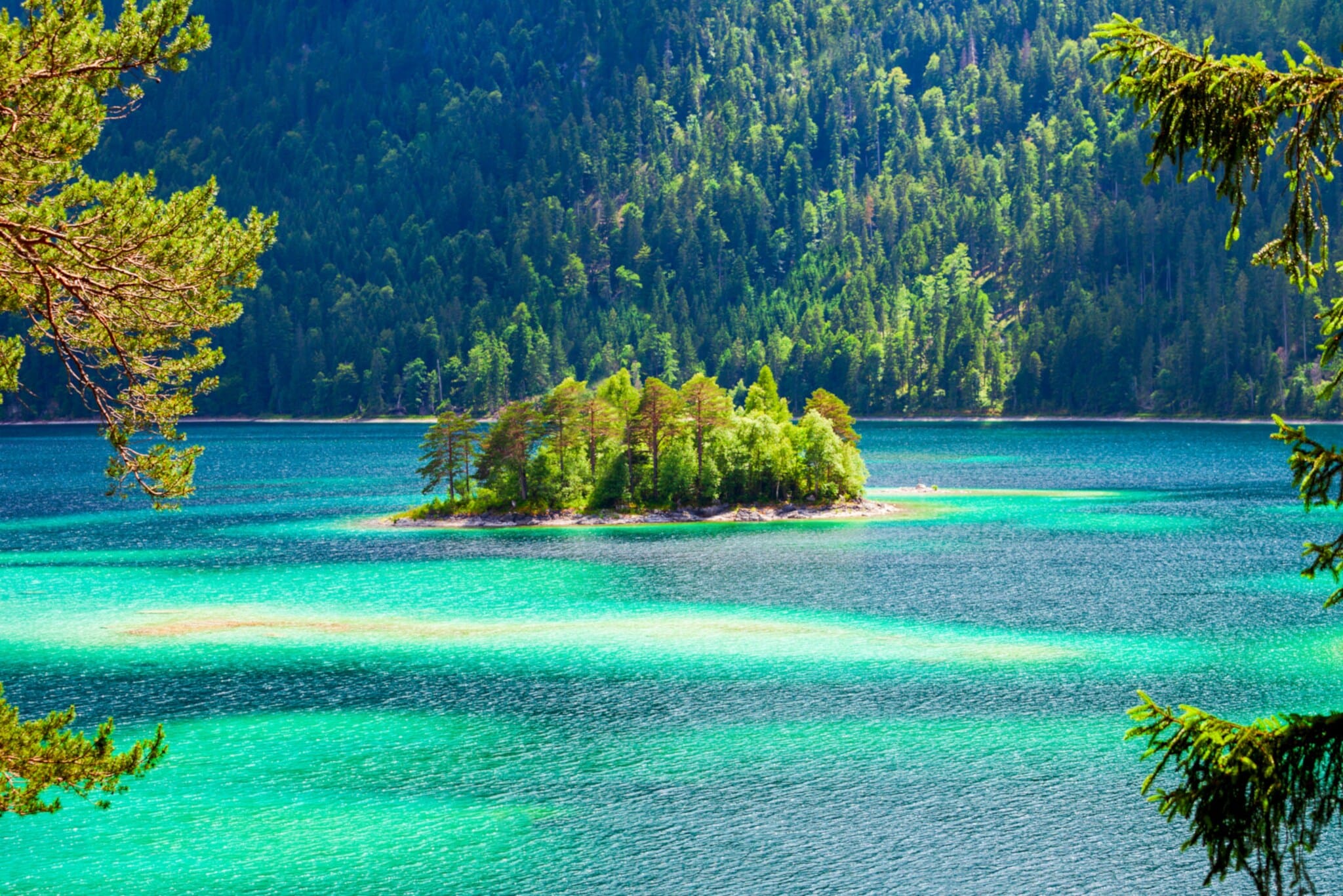 Ein See in verschiedenen Türkis- und Blautönen, in der Mitte eine kleine Insel und im Hintergrund ein Wald. Ein See in verschiedenen Türkis- und Blautönen, in der Mitte eine kleine Insel und im Hintergrund ein Wald.