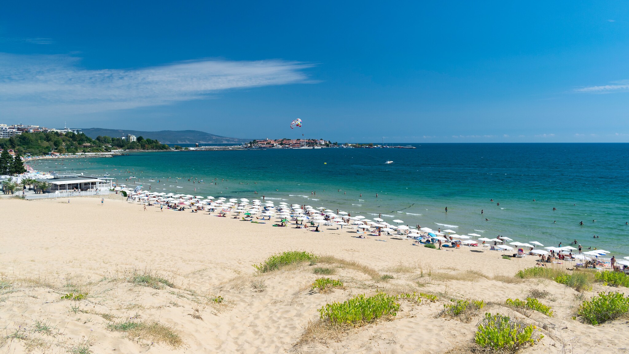 Sonnenliegen an einem Sandstrand mit Dünen in einer Bucht mit türkisblauem Meer.