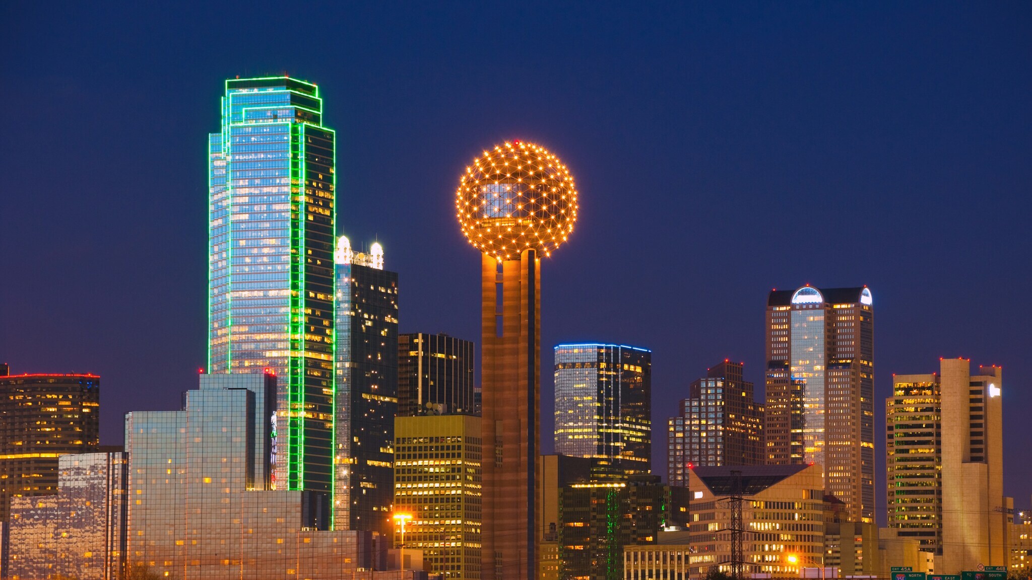 Erleuchtete Skyline von Dallas mit Wolkenkratzern und Gebäude mit kugelförmiger Spitze bei Dunkelheit.