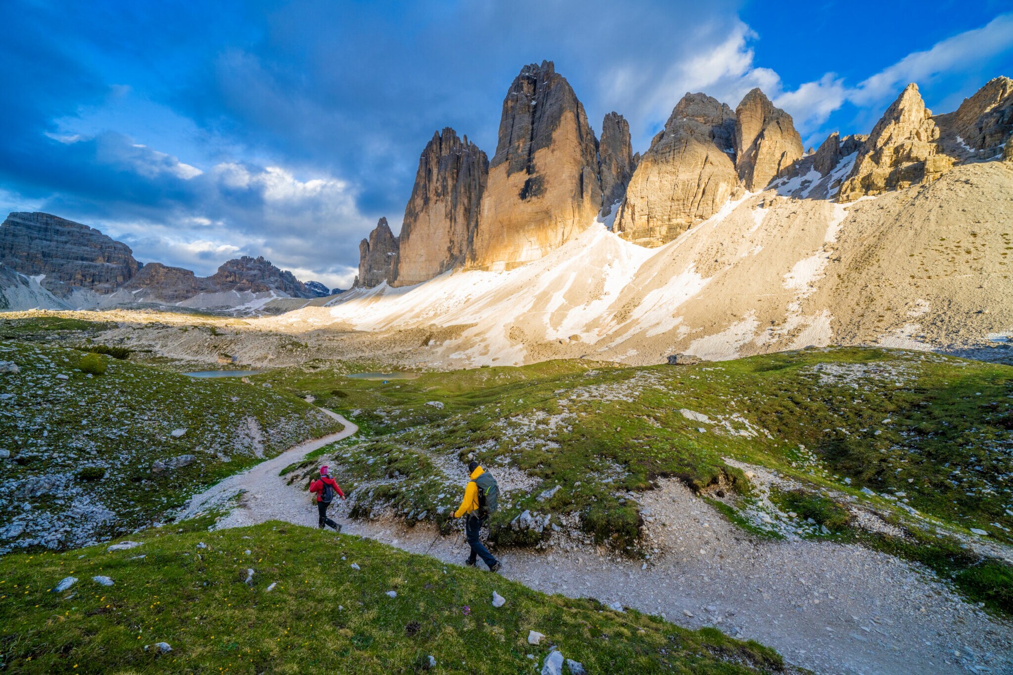 Zwei Personen beim Wandern, im Hintergrund Berge, blauer Himmel und Wolken.