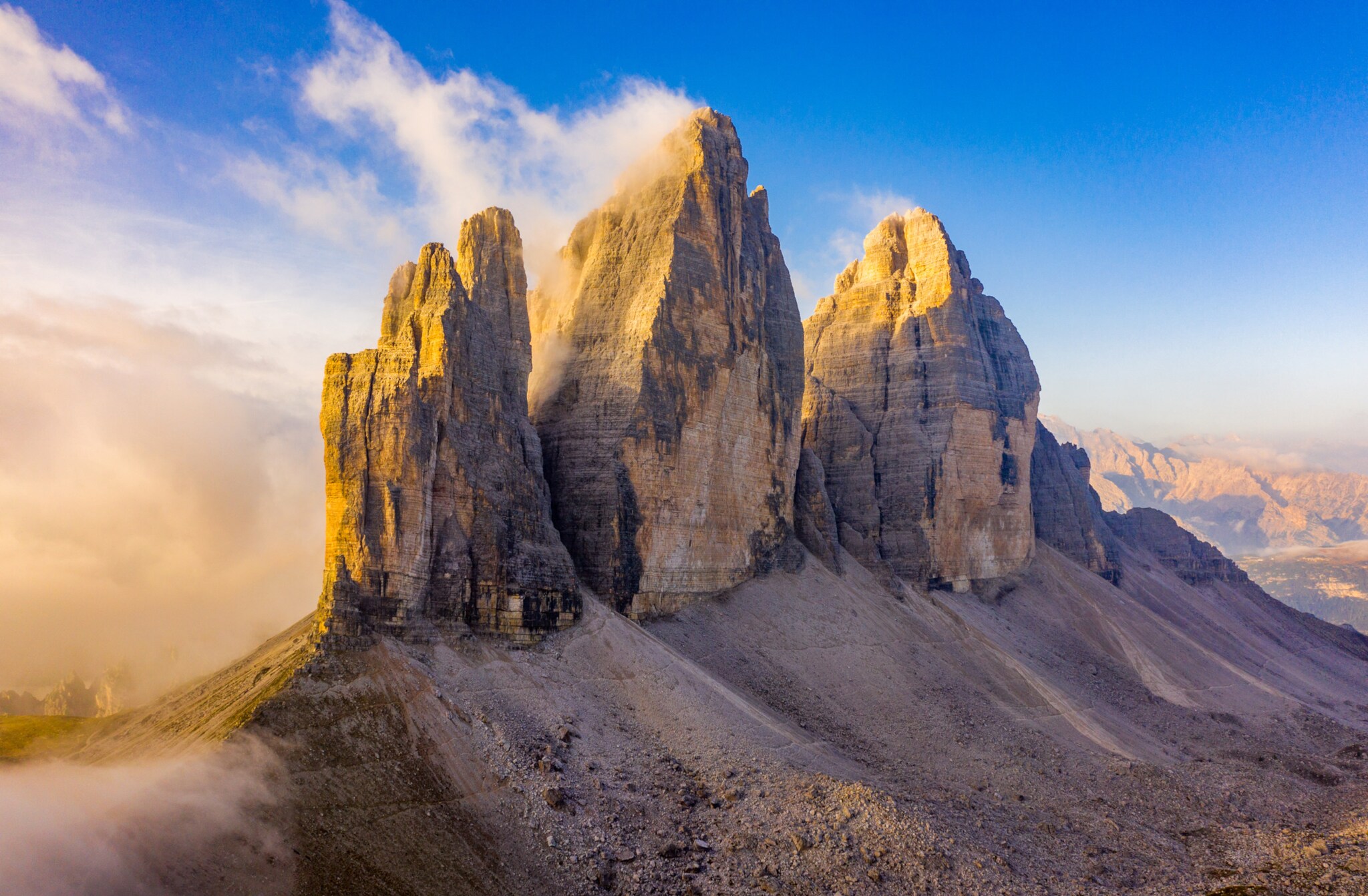 Blick auf drei markante Felstürme der Dolomiten im Sonnenschein, im Hintergrund blauer Himmel.