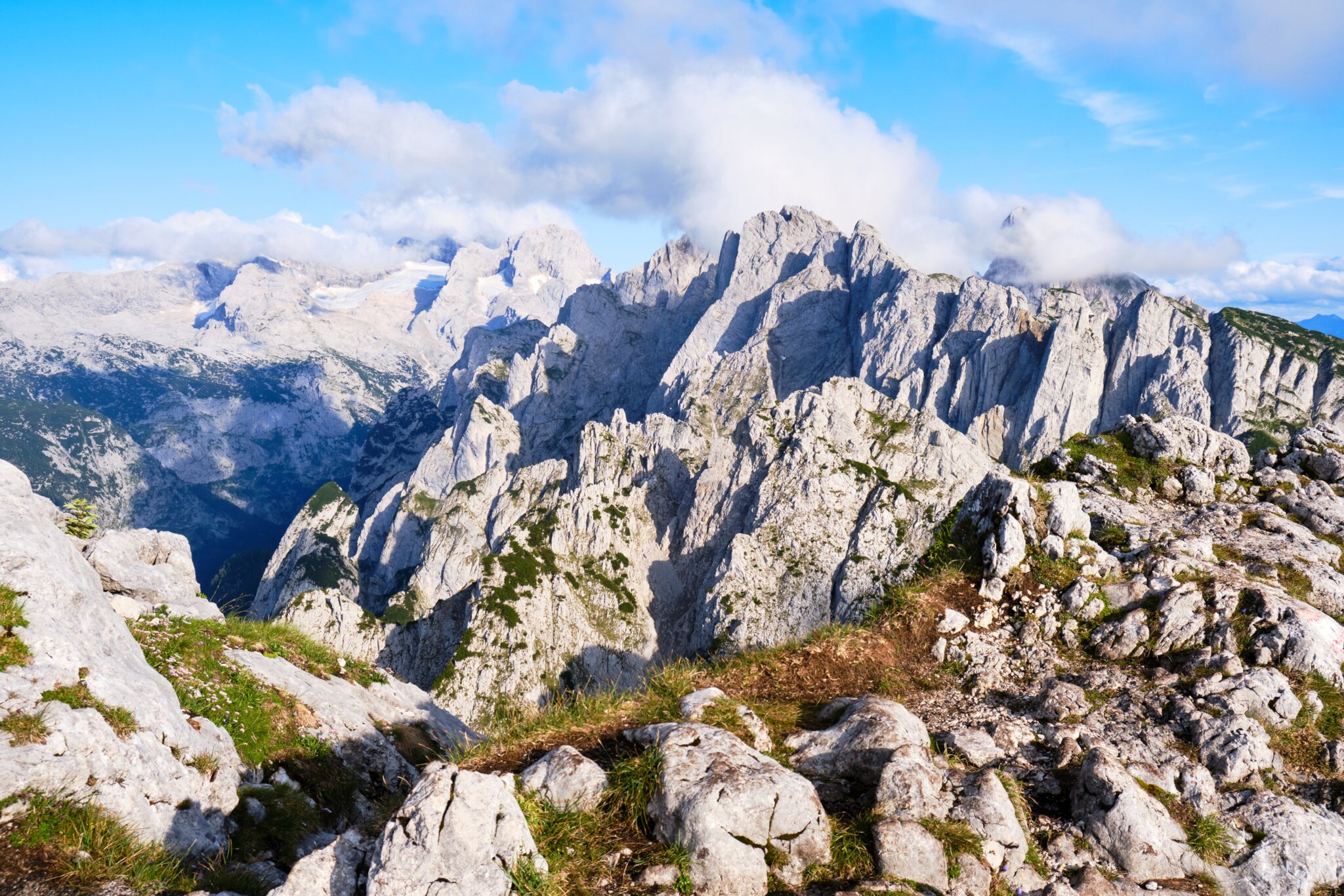 Blick auf teils begrünte Berggipfel und blauen Himmel mit weißen Wolken.