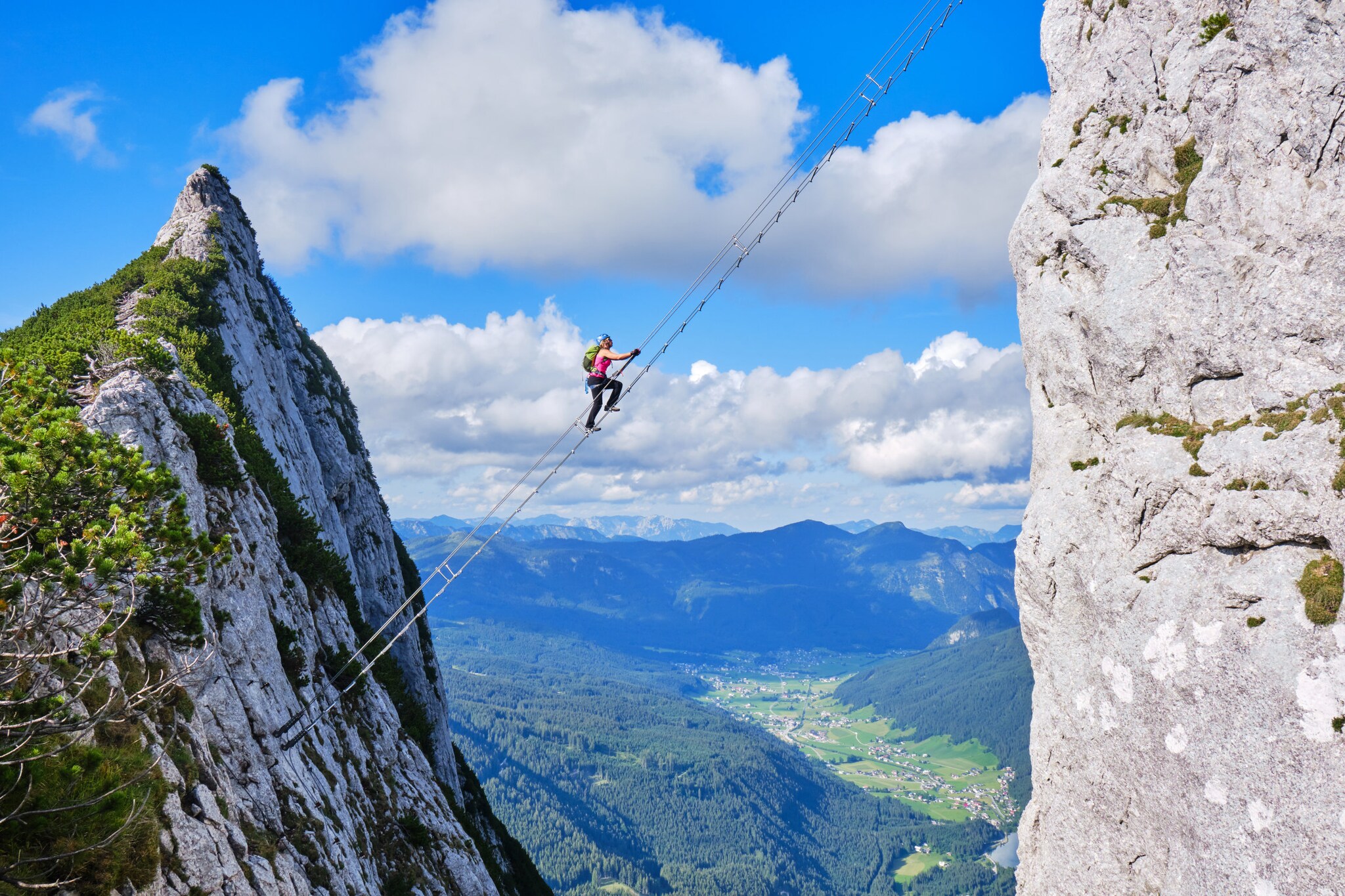 Eine Person auf einer Leiter zwischen zwei Felsen über einem grünen Tal. Eine Person auf einer Leiter zwischen zwei Felsen über einem grünen Tal.