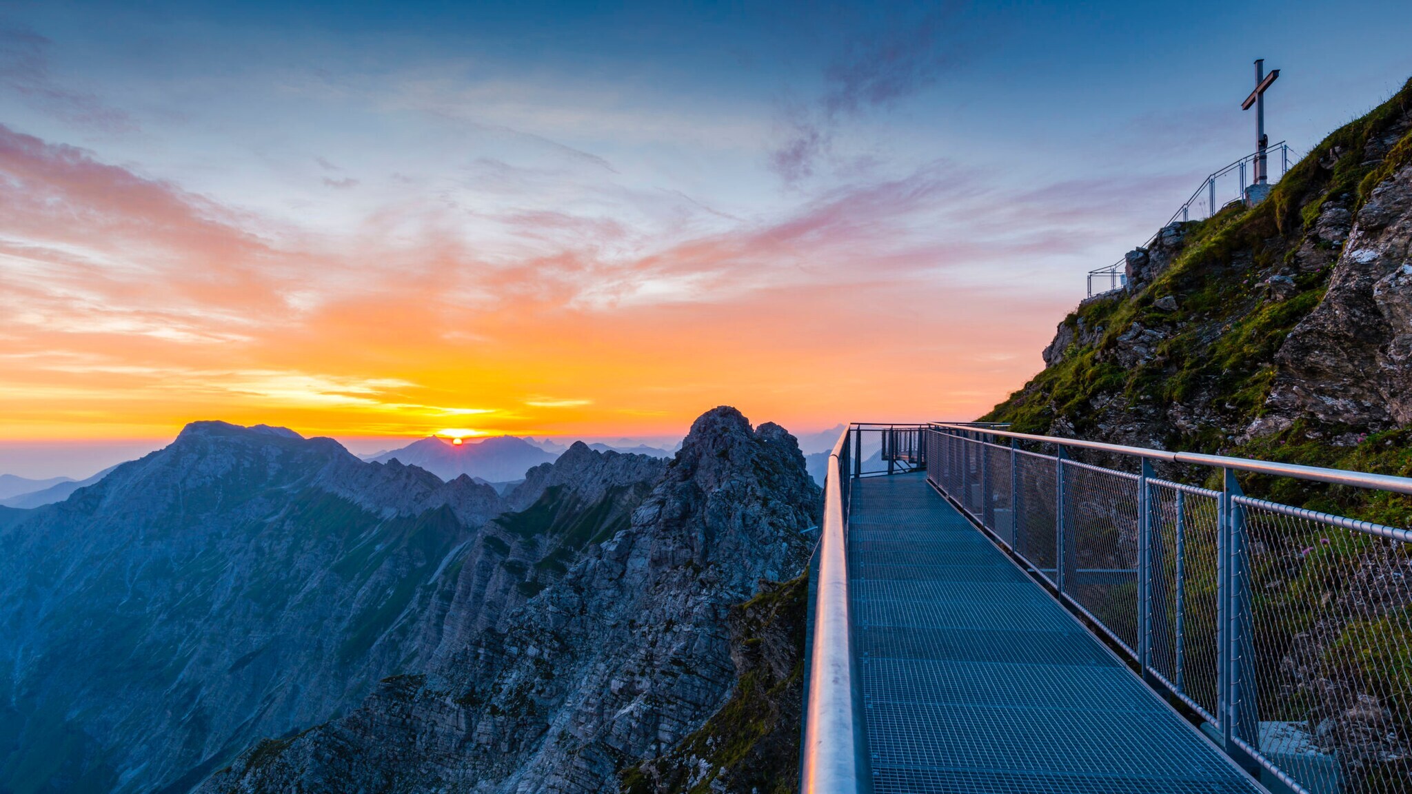 Aussichtsplattform und Gipfelkreuz des Nebelshorns bei Sonnenaufgang.