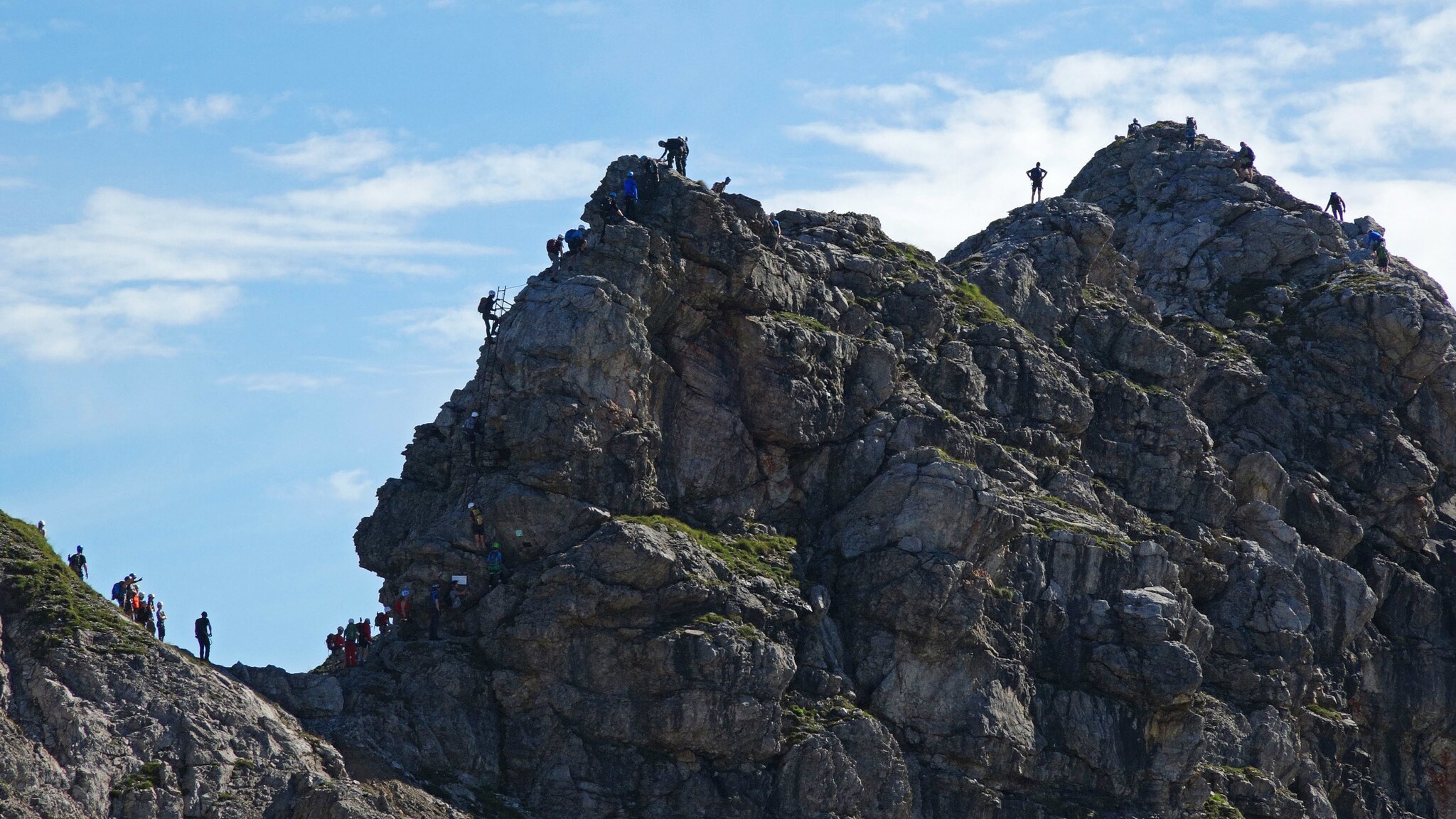Mehrere Personen, die einen Felsen am Hindelanger Klettersteig erklimmen. Mehrere Personen, die einen Felsen am Hindelanger Klettersteig erklimmen.