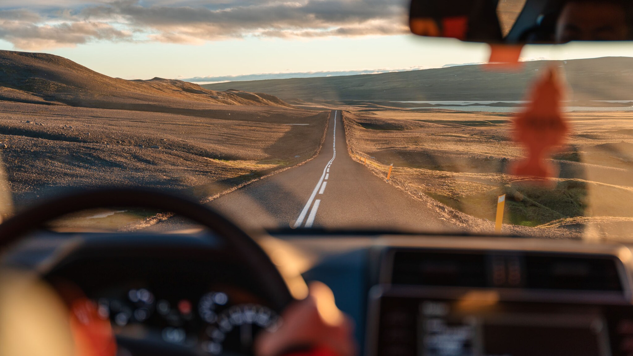 Blick auf eine Landstraße in karger, hügeliger Naturlandschaft durch die Windschutzscheibe eines fahrenden Autos.
