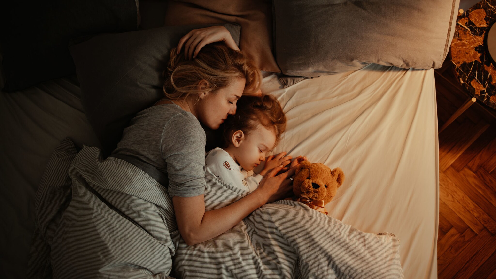 Eine Frau und ein Kind liegen aneinandergekuschelt mit einem Teddy im Bett. Eine Frau und ein Kind liegen aneinandergekuschelt mit einem Teddy im Bett.