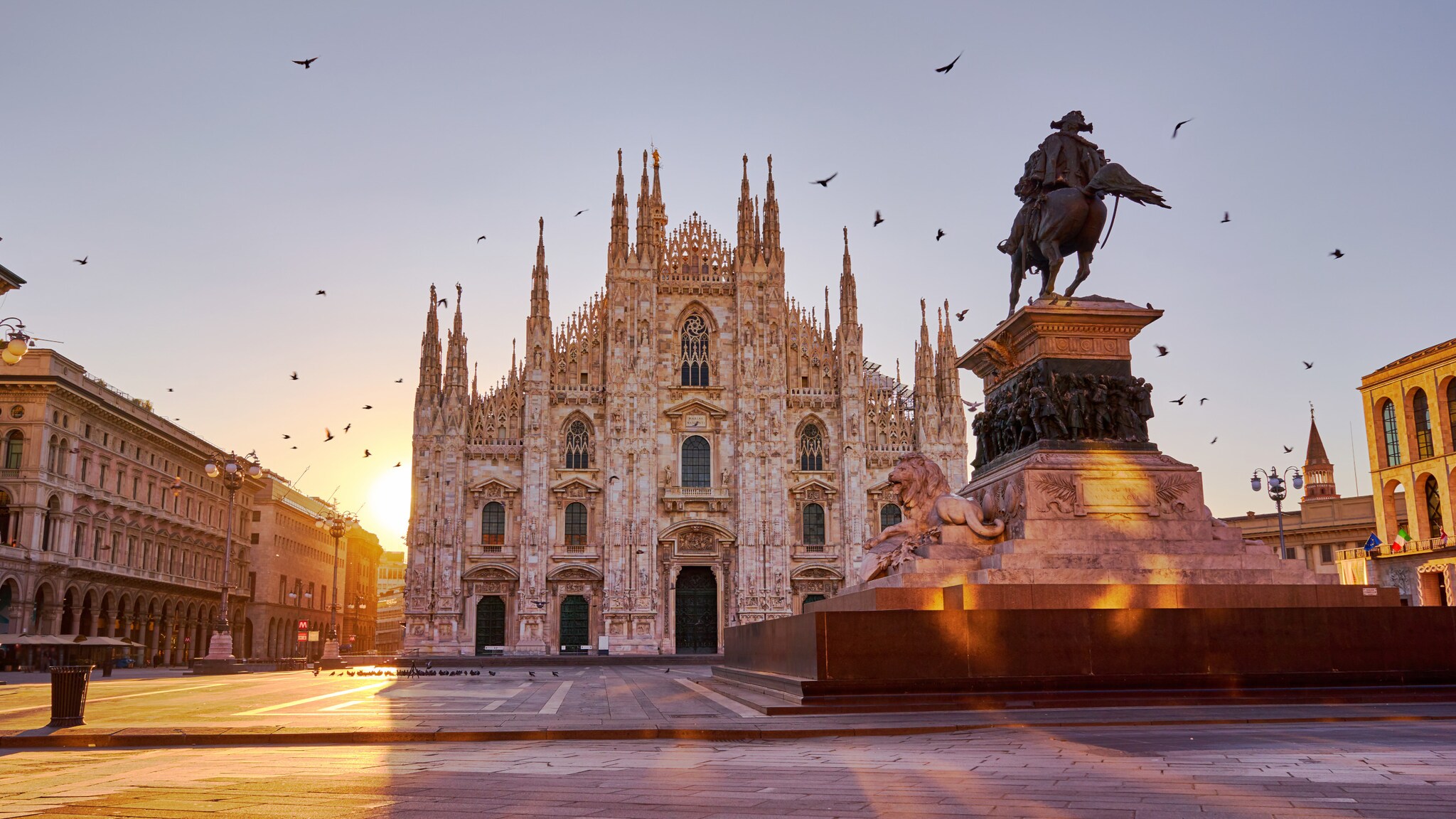 Mailänder Dom im gotischen Stil mit menschenleerem Platz und Reiterstatue im Vordergrund bei warmem Sonnenlicht.