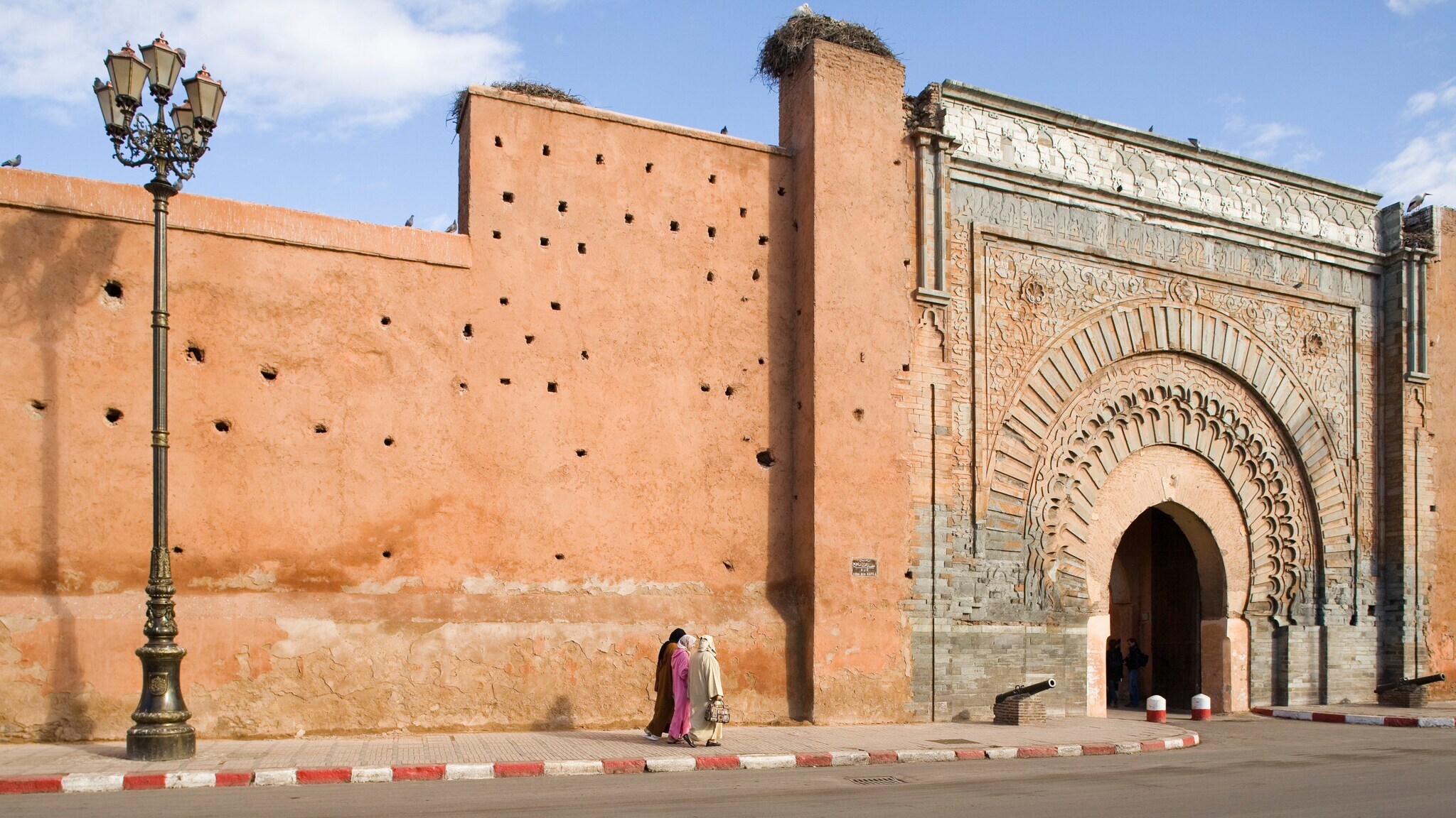 Stadtmauer aus rötlichem Stein mit verziertem Torbogen.