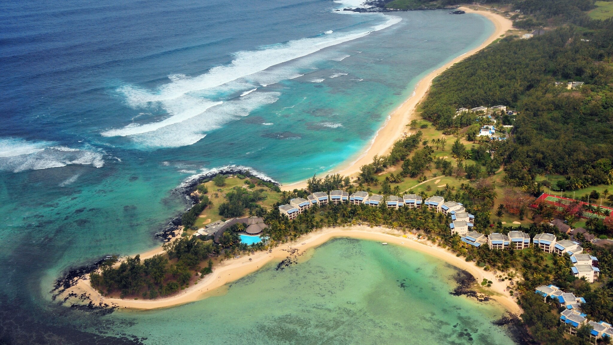 Luftaufnahme eines Küstenabschnitts mit Hotelresort inmitten tropischer Natur auf einer Landzunge mit Sandstrand, umgeben von türkisblauem Meer. Luftaufnahme eines Küstenabschnitts mit Hotelresort inmitten tropischer Natur auf einer Landzunge mit Sandstrand, umgeben von türkisblauem Meer.