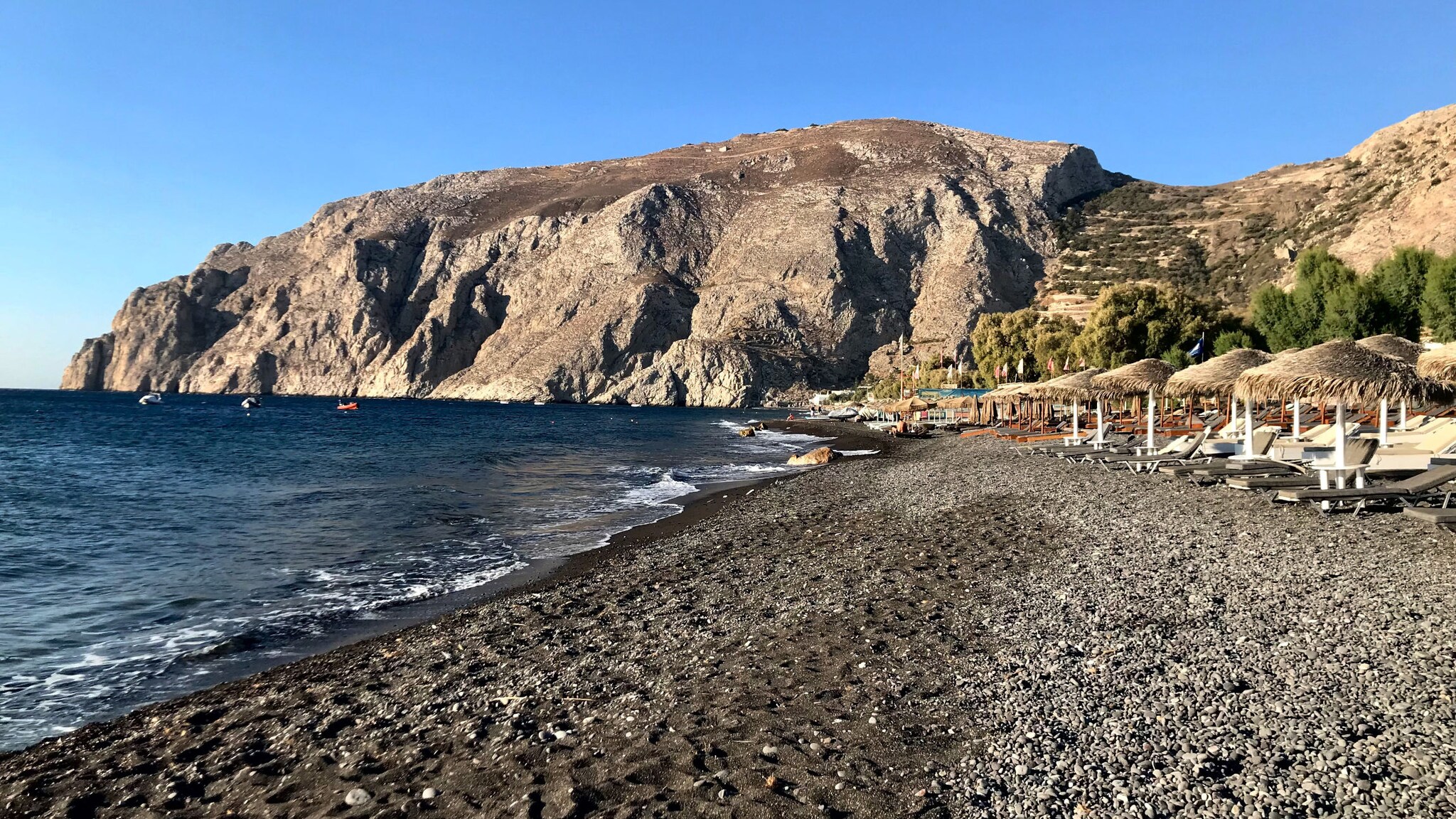 Schwarzer Sandstrand mit Sonnenliegen an einer Felsküste.