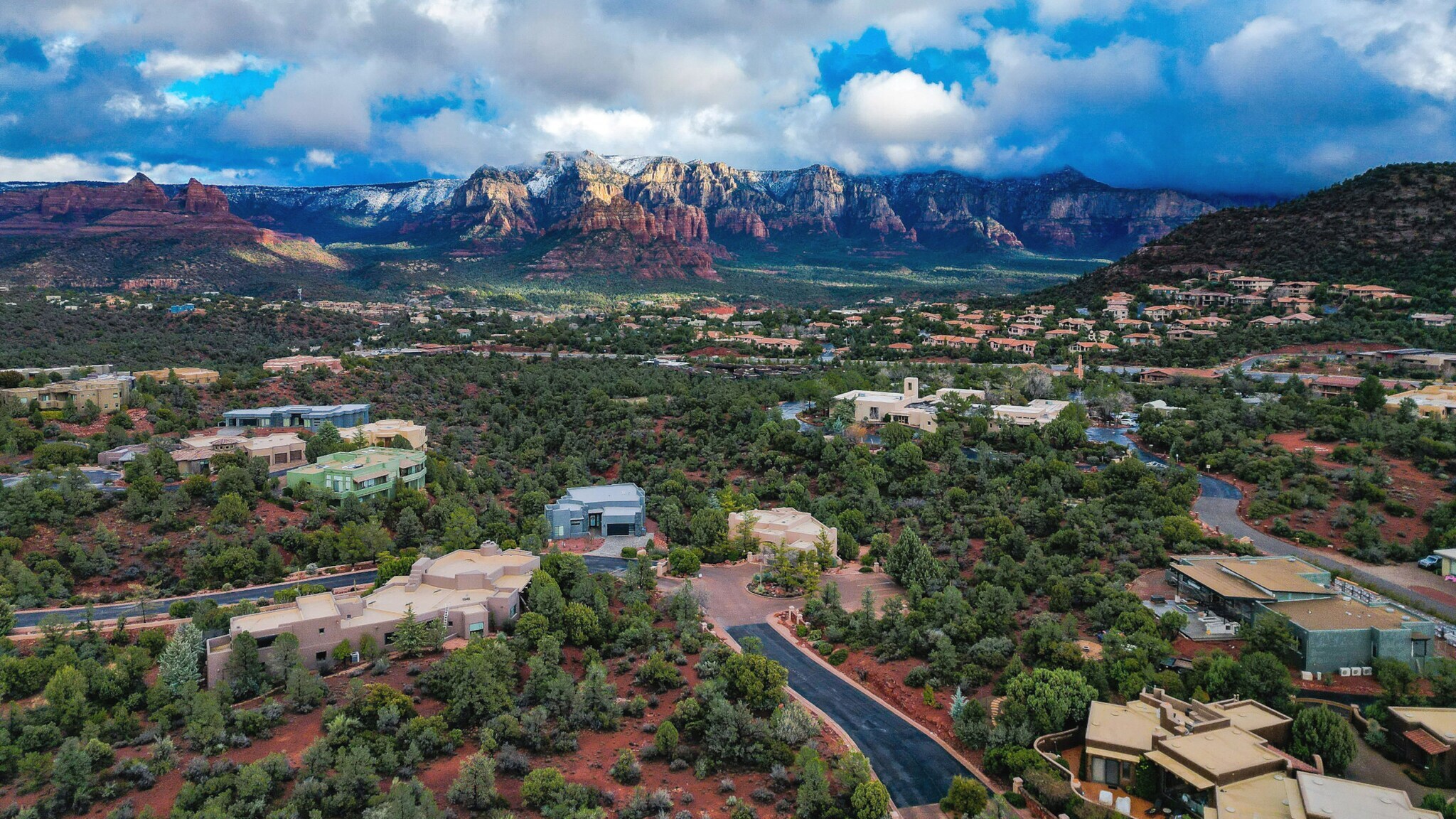 Häuser in Wüstenlandschaft mit grünen Büschen vor Gebirgszug im Hintergrund.