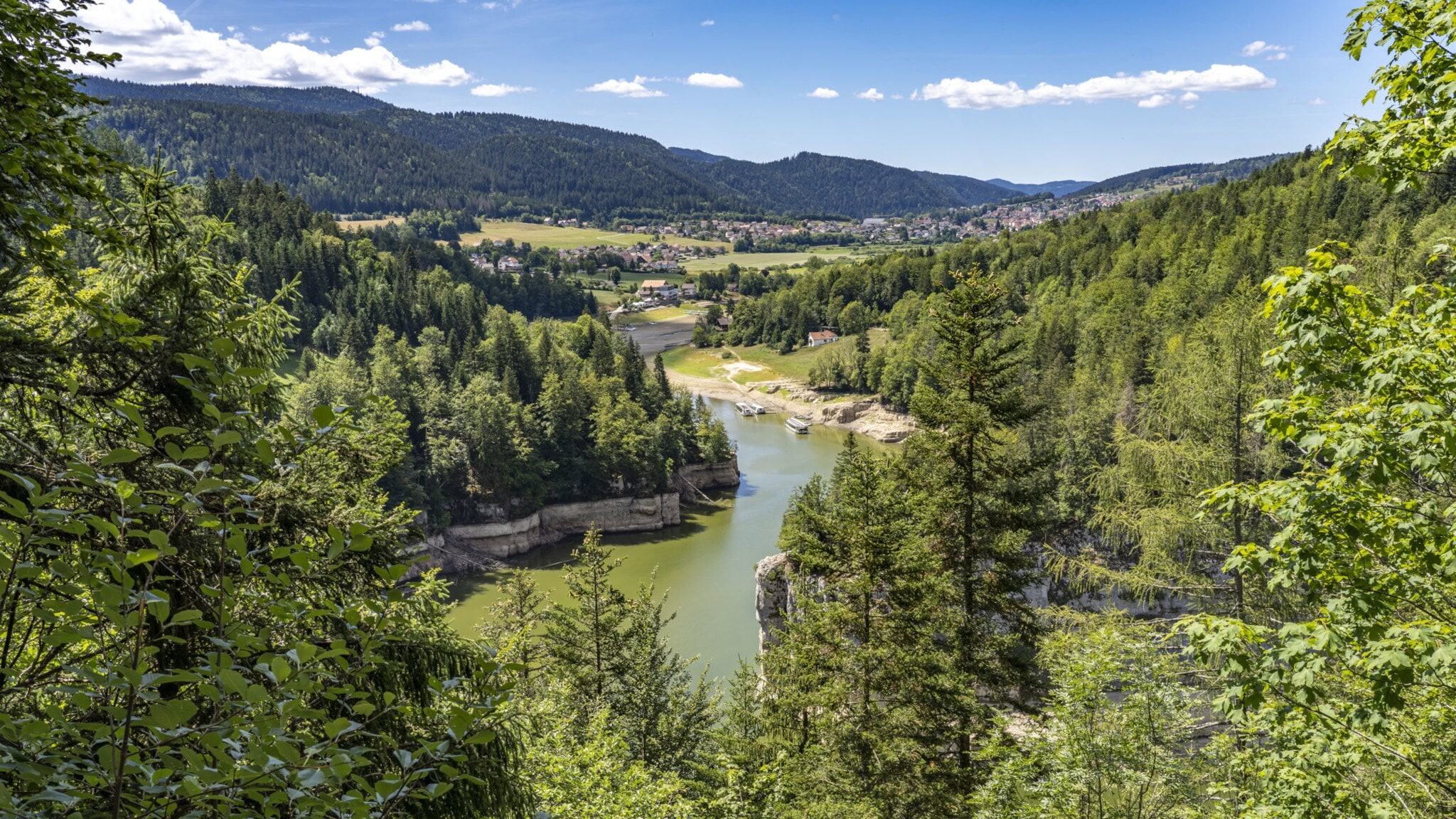 Der Fluss Doubs an der Grenze zwischen Frankreich und der Schweiz mit Bergen im Hintergrund und grünen Bäumen im Vordergrund. Der Fluss Doubs an der Grenze zwischen Frankreich und der Schweiz mit Bergen im Hintergrund und grünen Bäumen im Vordergrund.