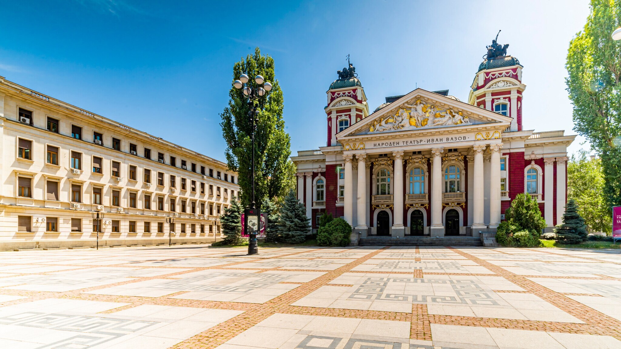 Historisches Theatergebäude mit Dreiecksgiebel und Säulen am Eingangsbereich an einem Platz.