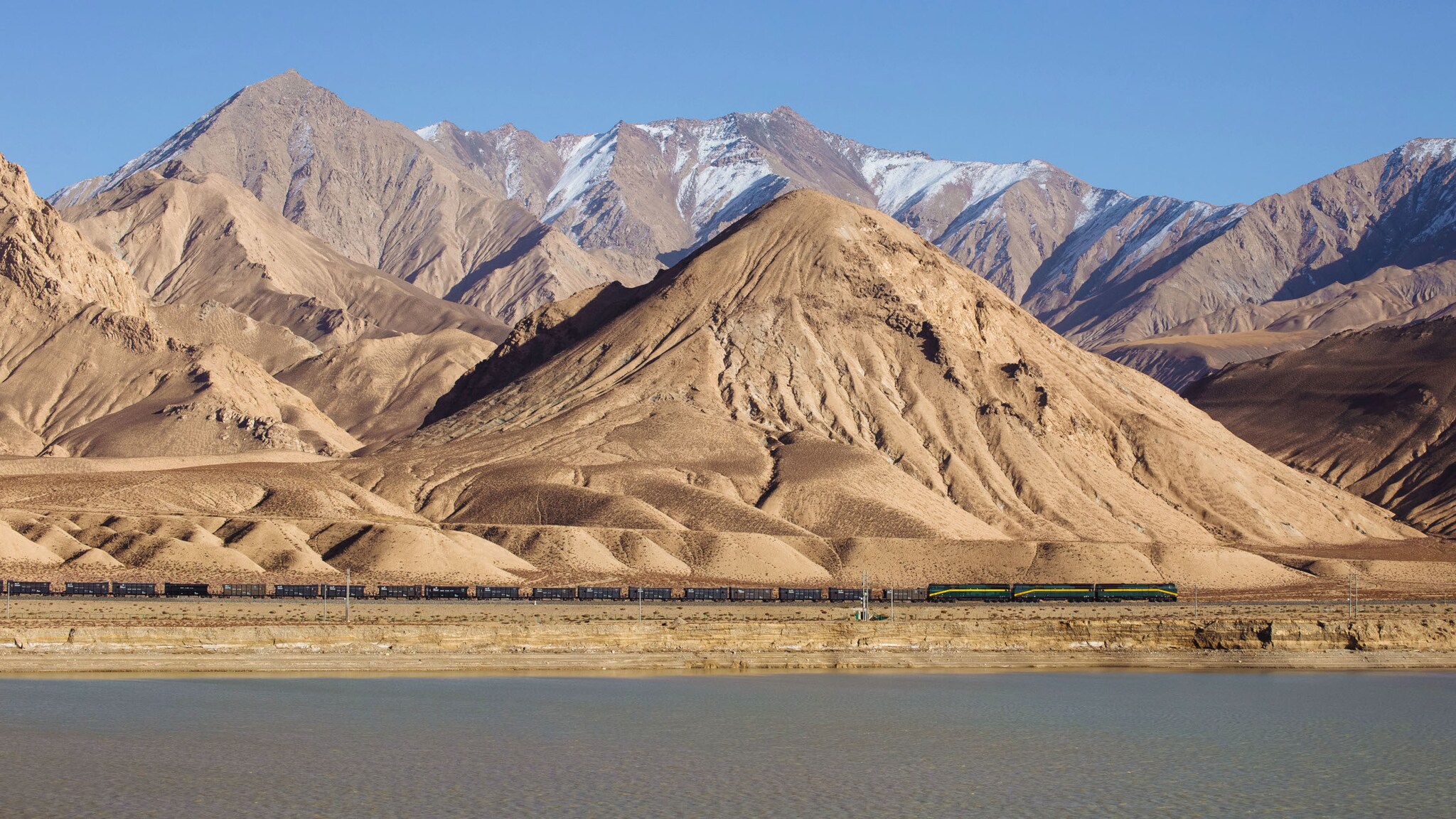 Ein Zug fährt am Fuße einer kargen Berglandschaft in Sandtönen. Ein Zug fährt am Fuße einer kargen Berglandschaft in Sandtönen.