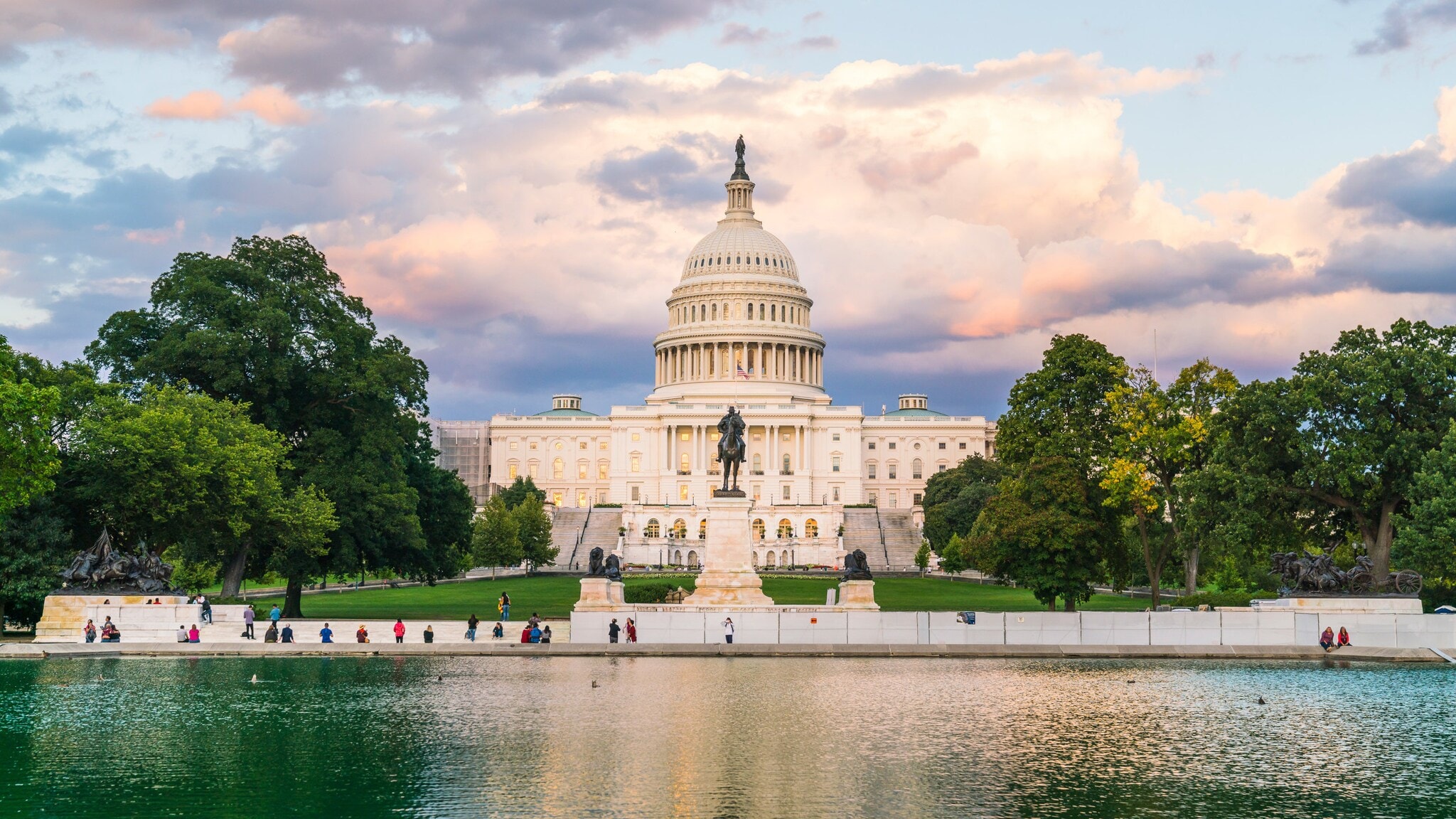 Gebäude im neoklassizistischen Stil mit Rotunde, im Vordergrund Personen an einem Teich in einer Parkanlage. Gebäude im neoklassizistischen Stil mit Rotunde, im Vordergrund Personen an einem Teich in einer Parkanlage.