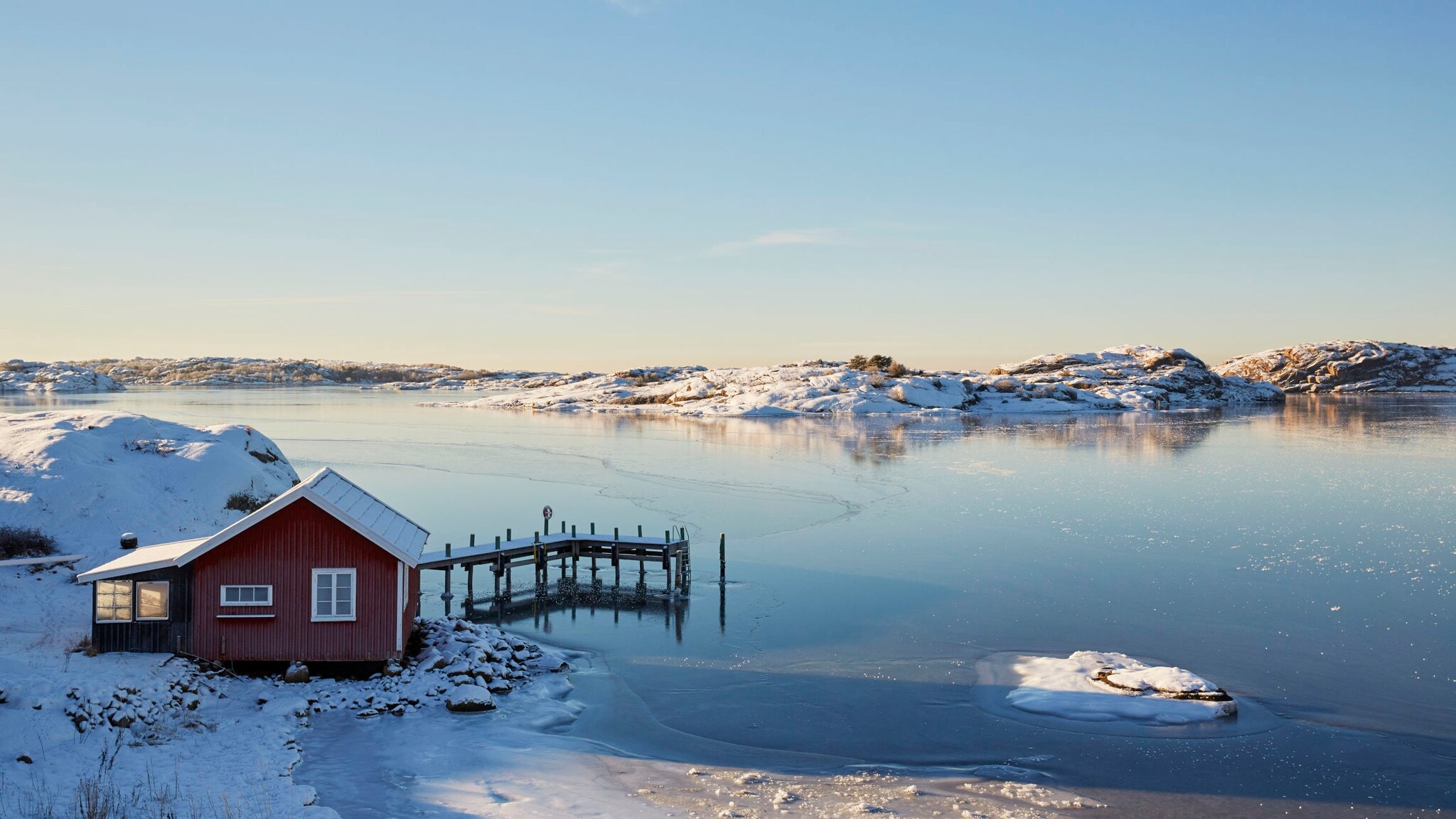 Ein rotes Holzhaus mit Steg an einem zugefrorenen See in verschneiter Landschaft in Schweden. Ein rotes Holzhaus mit Steg an einem zugefrorenen See in verschneiter Landschaft in Schweden.