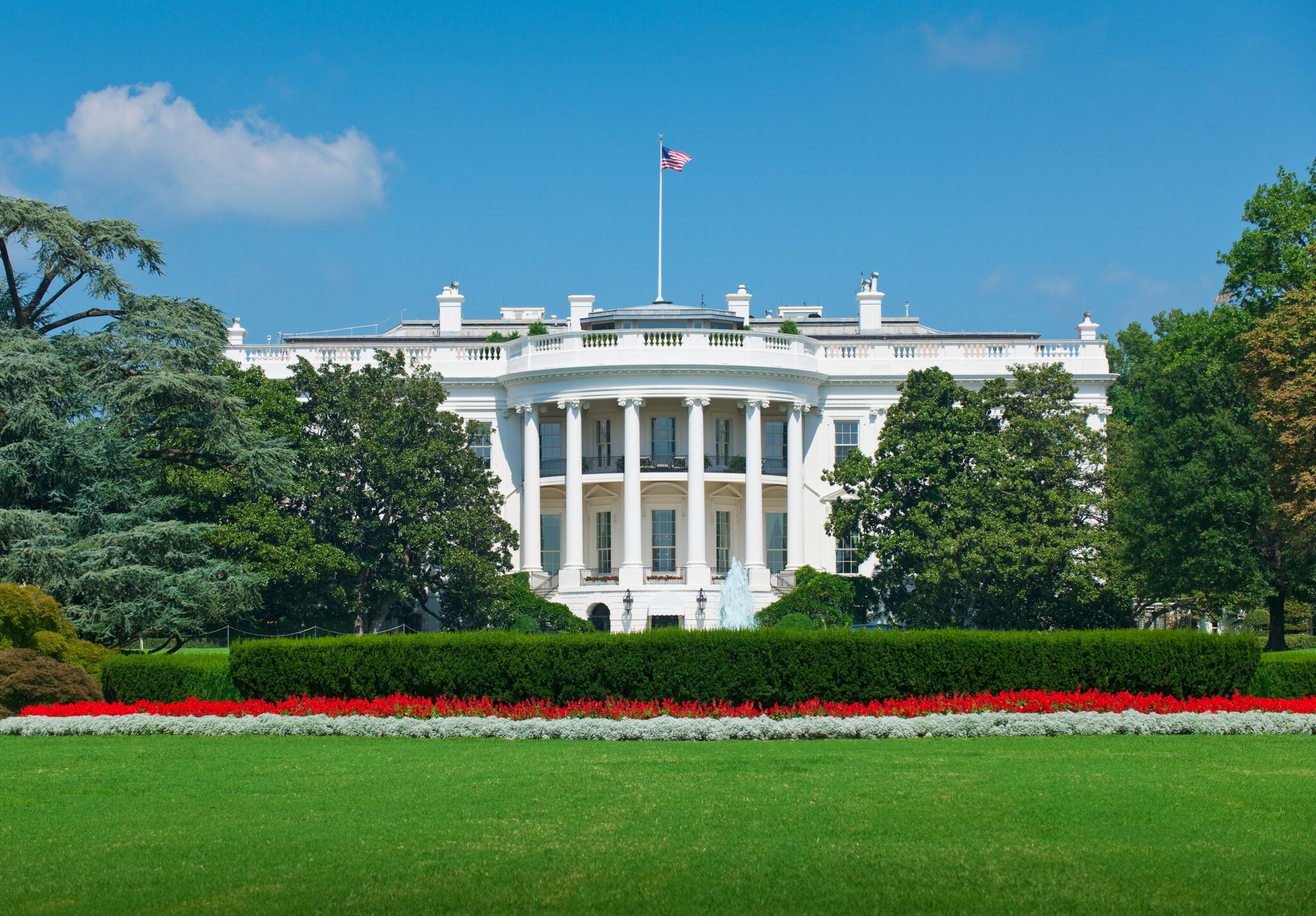 Weißes Haus im klassizistischen Stil mit US-Flagge, umgeben von Parkanlage.