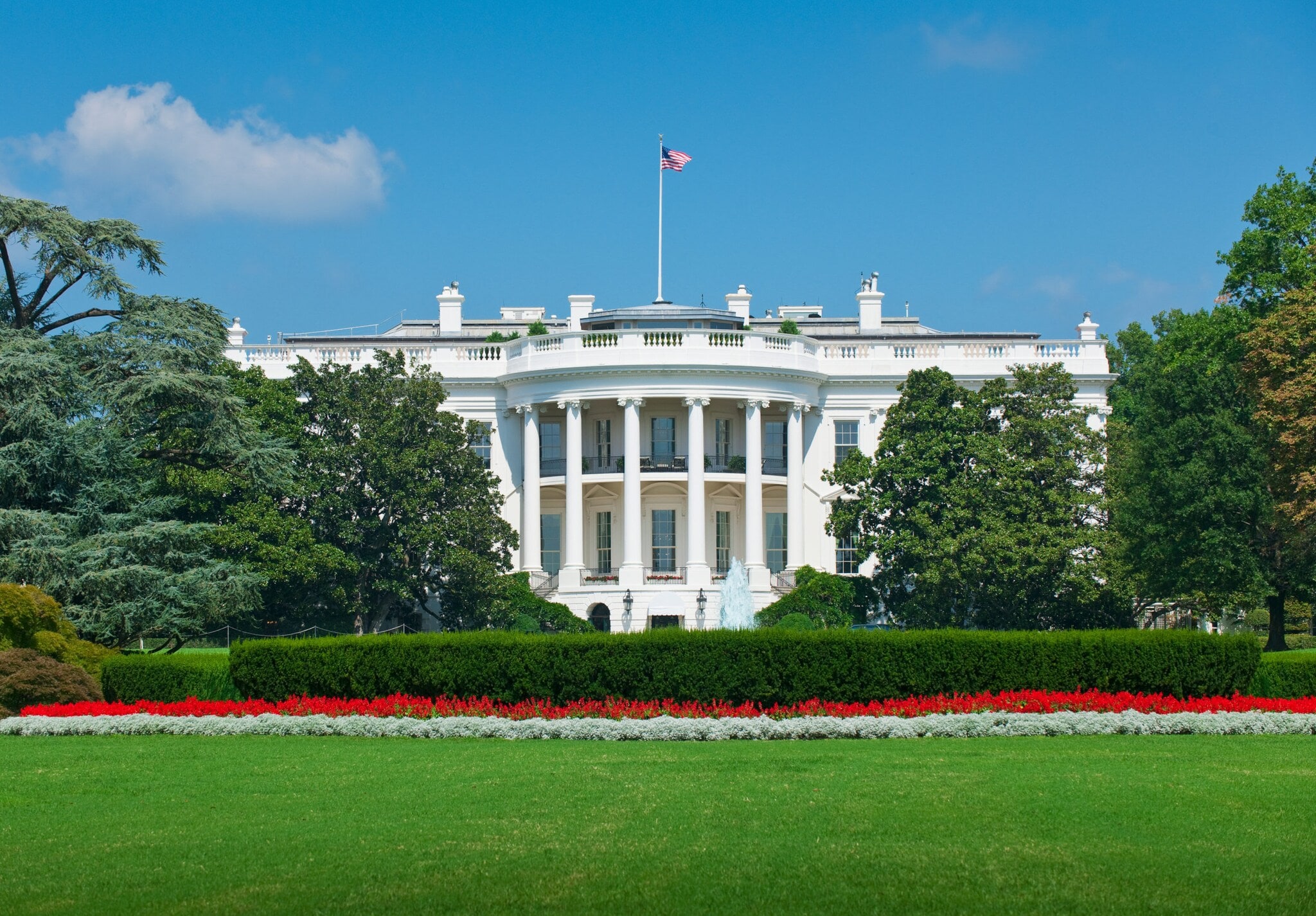 Weißes Haus im klassizistischen Stil mit US-Flagge, umgeben von Parkanlage. Weißes Haus im klassizistischen Stil mit US-Flagge, umgeben von Parkanlage.